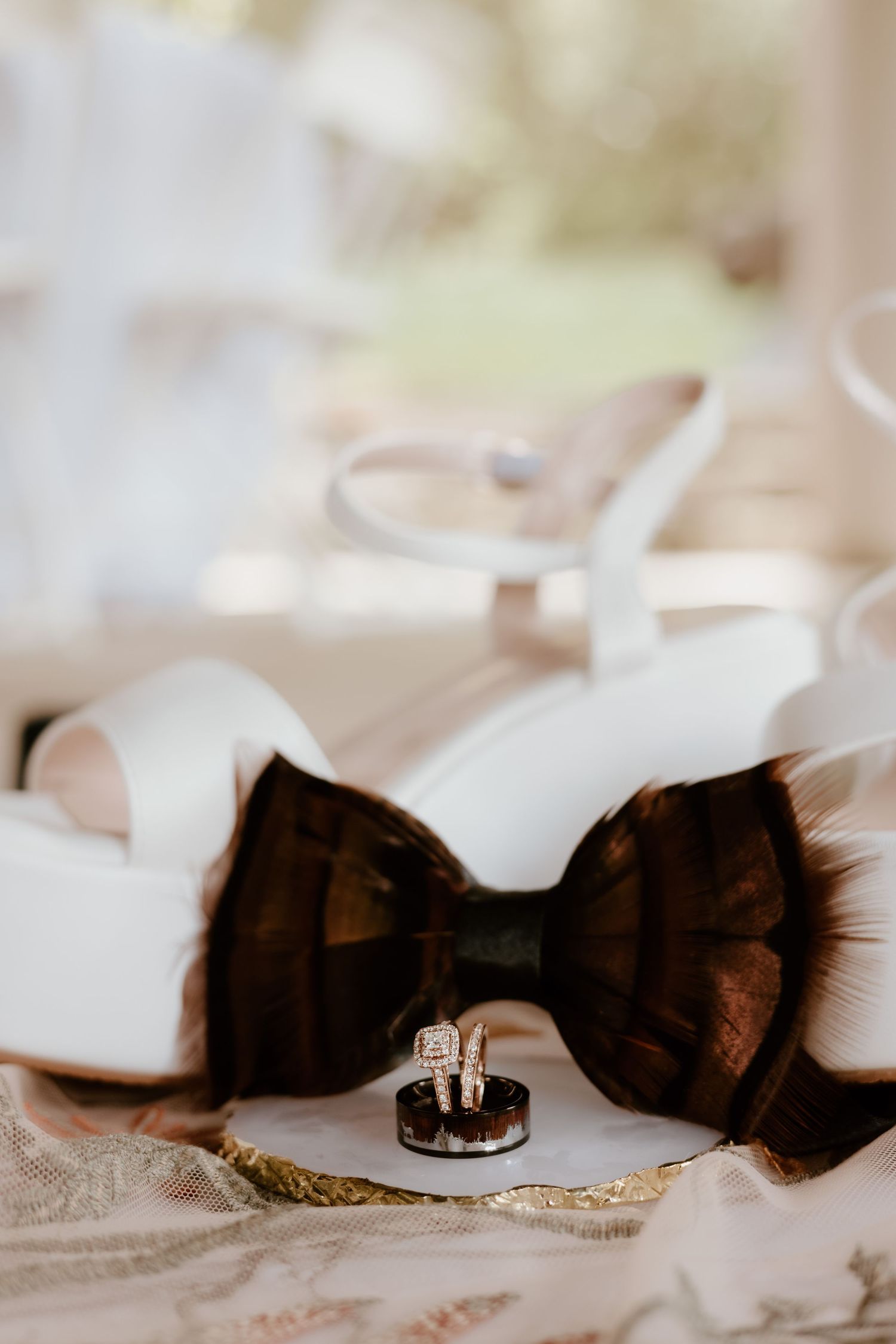 Wedding rings and black bow tie arranged artistically on delicate lace fabric in soft lighting.