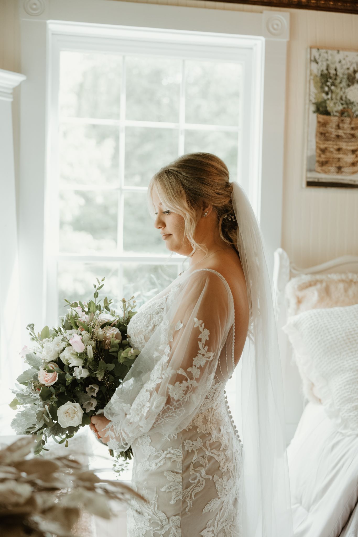 Ethereal bridal portrait series featuring a delicate lace wedding gown and flowing bouquet next to bright windows.