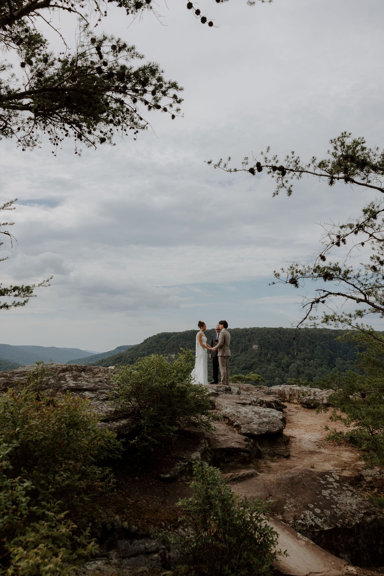 Bride and groom hold hands on a rocky overlook with sweeping mountain views during their outdoor elopement.
