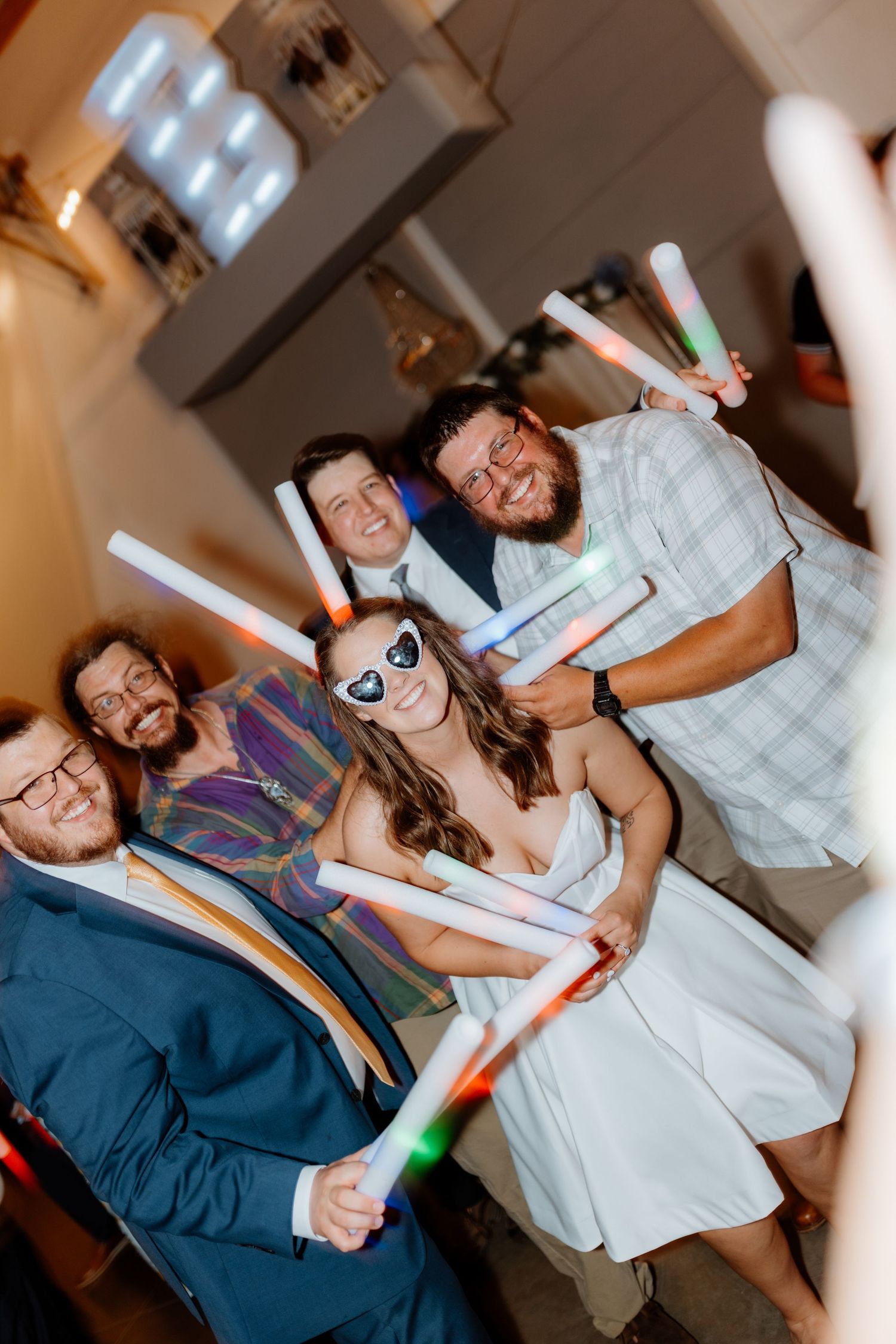 Group of wedding guests smiling and holding colorful glow sticks at a lively reception party.