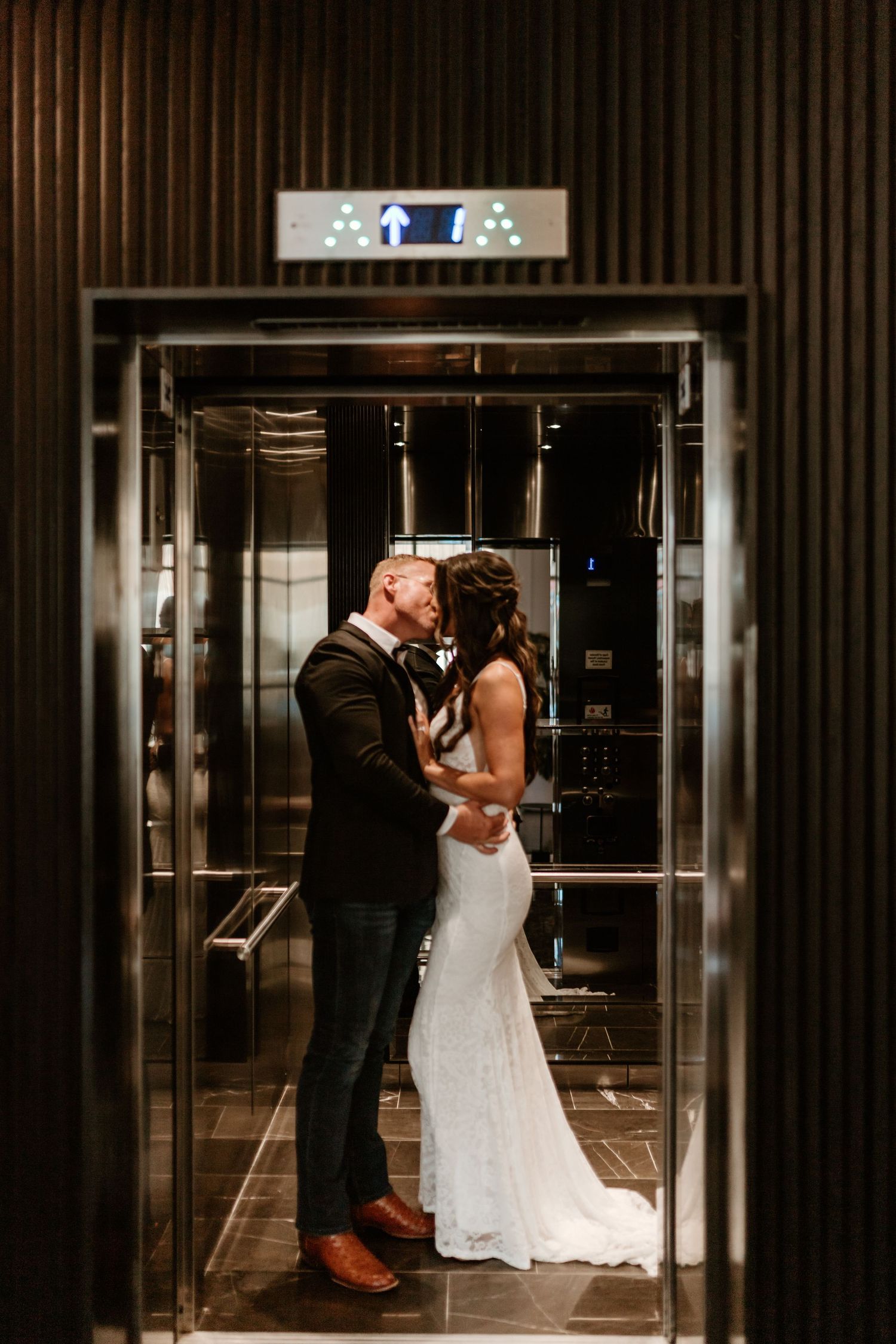 A romantic wedding moment captured in an elevator as a couple in formal attire embrace.