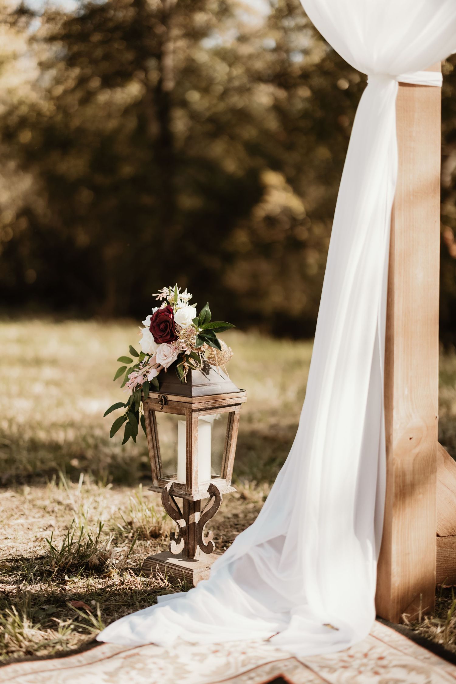 White fabric drapes elegantly on wooden posts creating a romantic outdoor ceremony setting with floral arrangements.