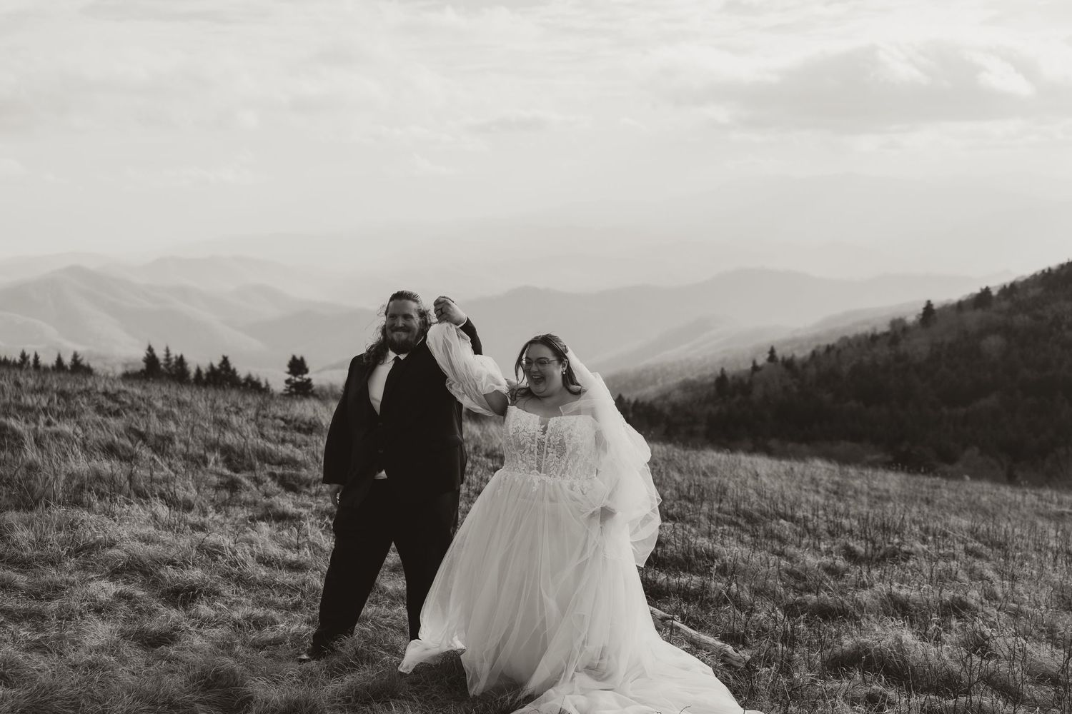 Bride and groom dancing on mountain meadow with scenic views in black and white wedding photo.