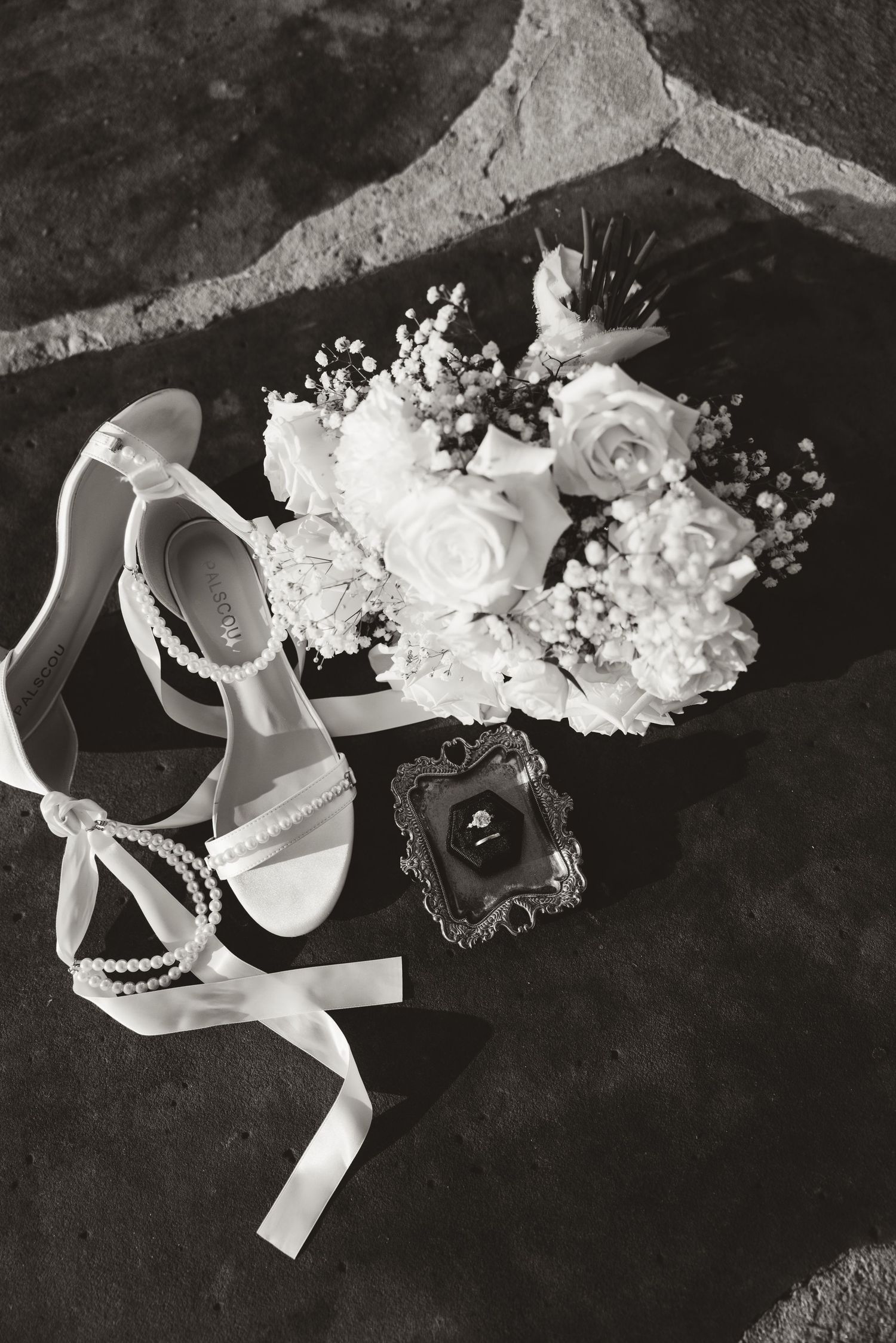 White bridal accessories including delicate floral headpiece and elegant heels arranged on dark background.