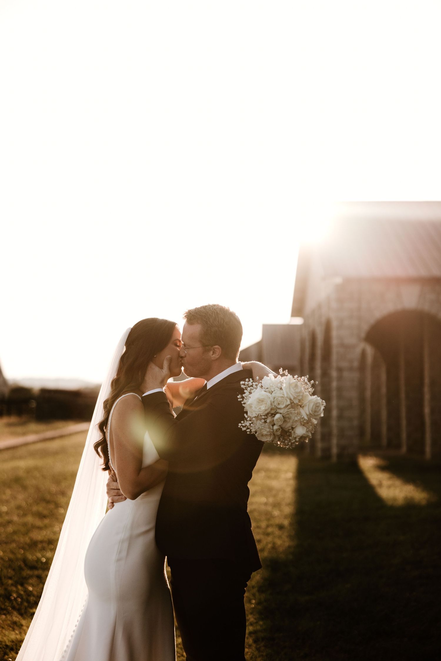 Romantic sunset wedding silhouette with couple embracing against golden light.