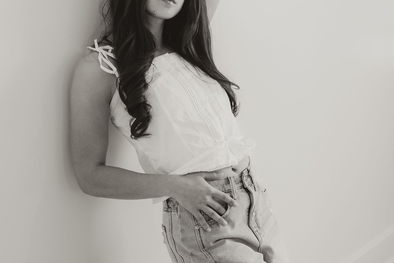 Black and white photo of a young woman in white top and denim shorts leaning against a wall.