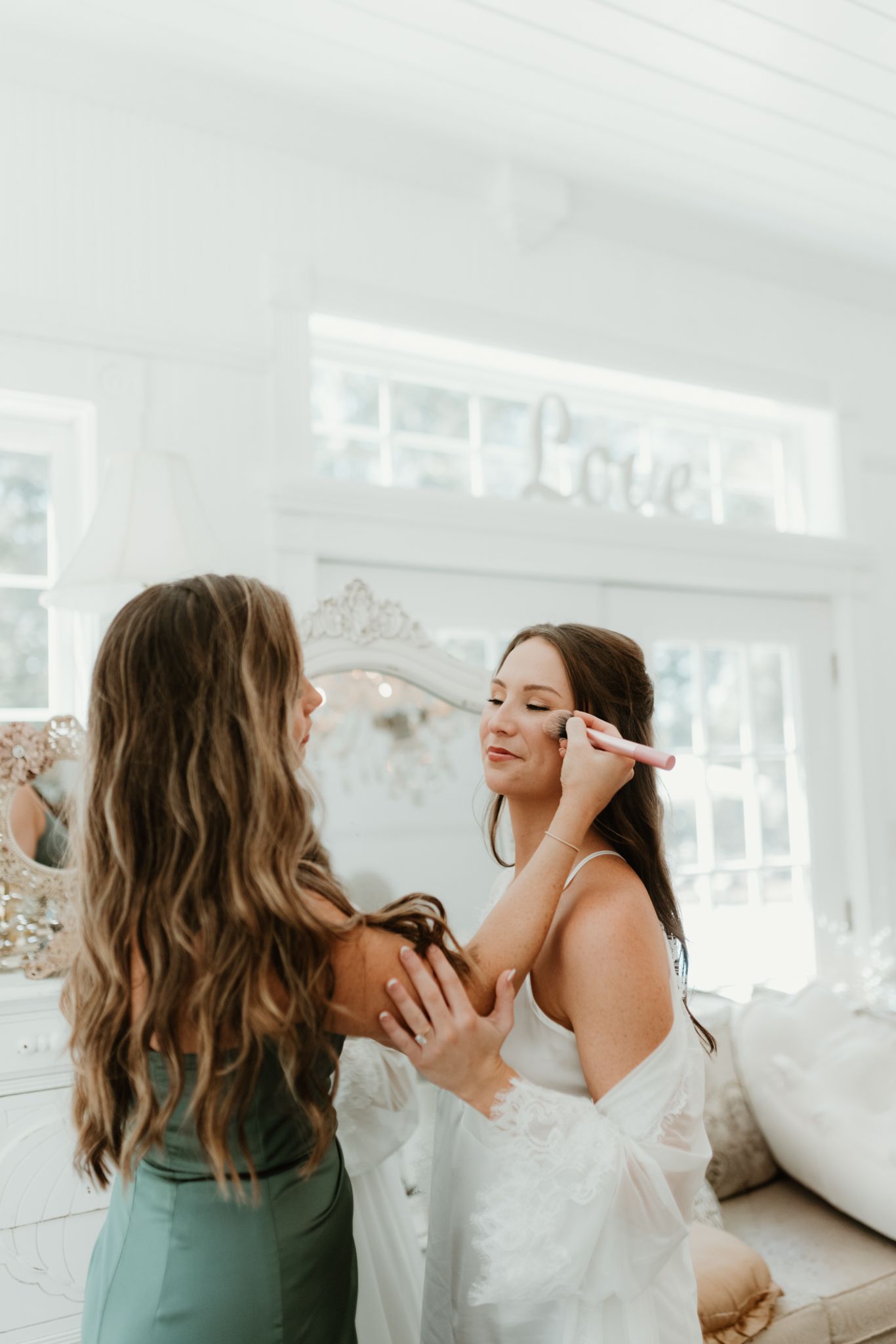 A makeup artist applying cosmetics during wedding preparations in a bright white room.