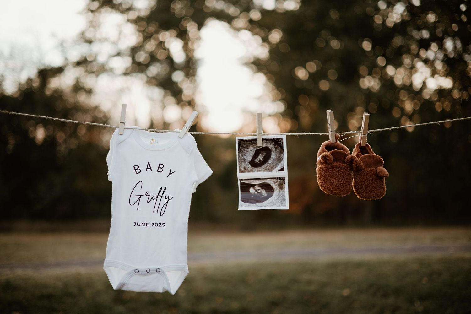Baby announcement items including a onesie, ultrasound photos, and tiny shoes displayed against sunset backdrop.