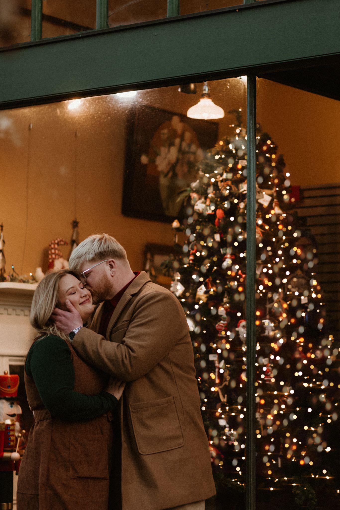 A romantic couple shares intimate holiday moments in front of a glowing Christmas tree.