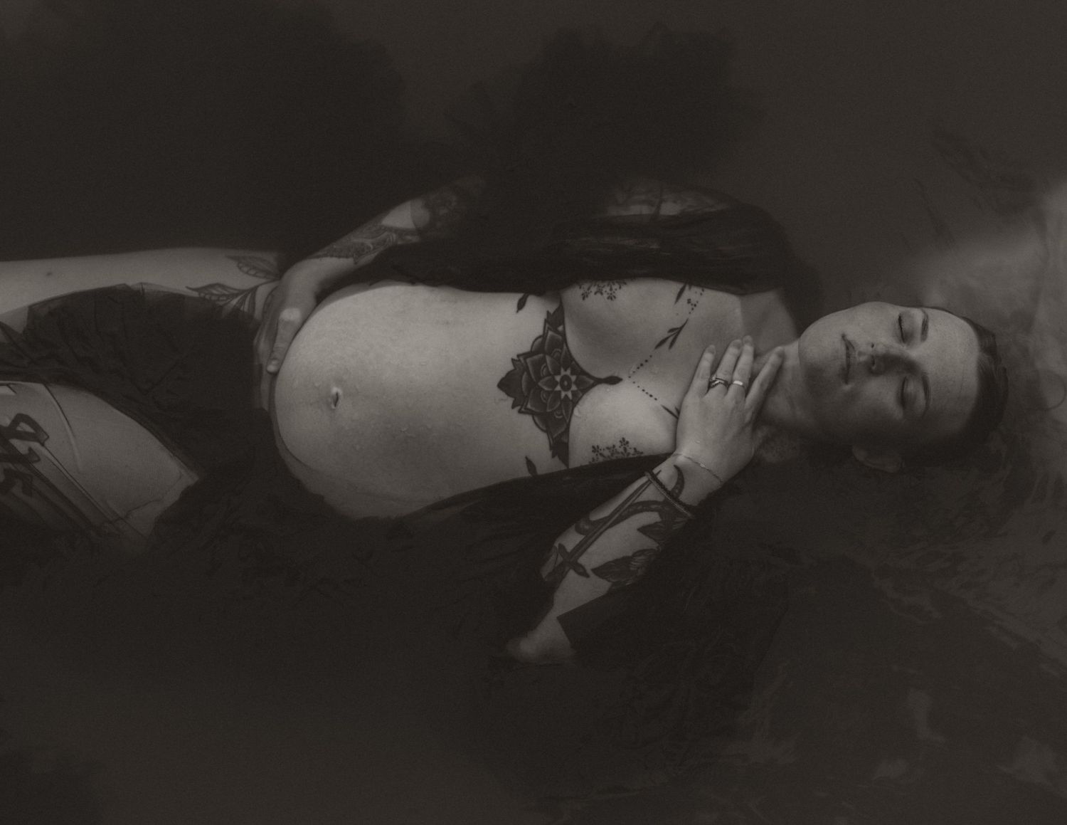 A black and white photograph of someone lying in dark water wearing black clothing and lingerie.