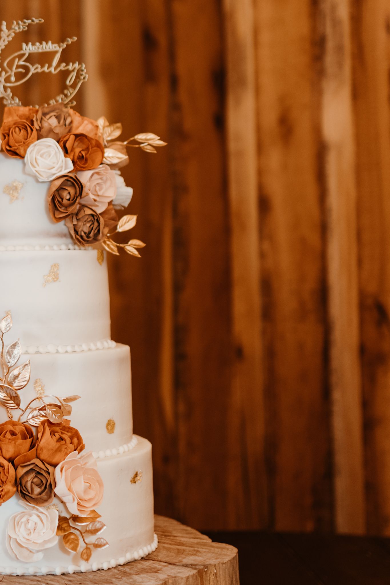 Elegant wedding cake with white frosting, rose gold flowers, and delicate pearl details on a rustic wooden backdrop.