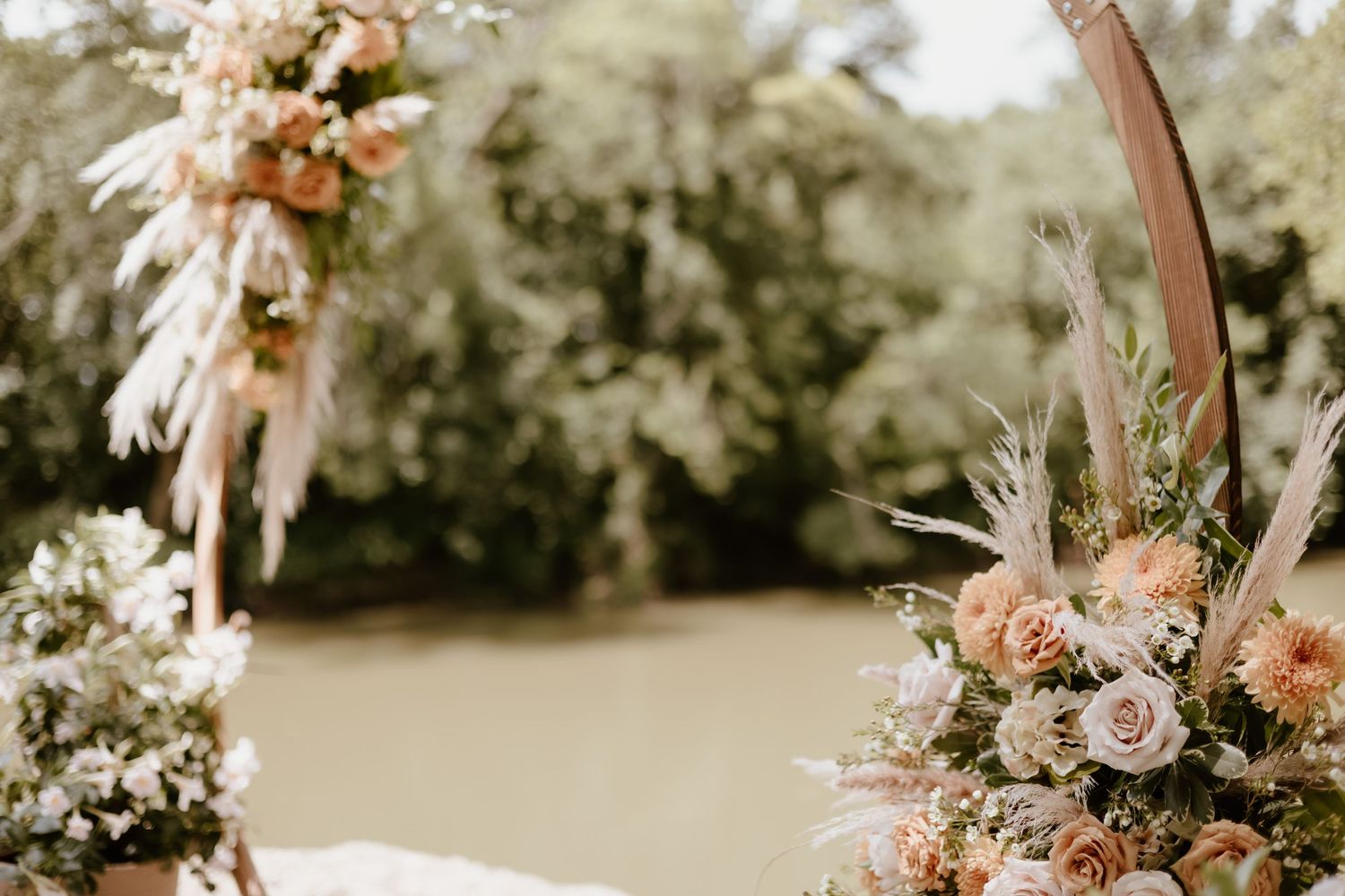 A romantic wedding arch decorated with soft pink and white flowers stands against a blurred outdoor background.