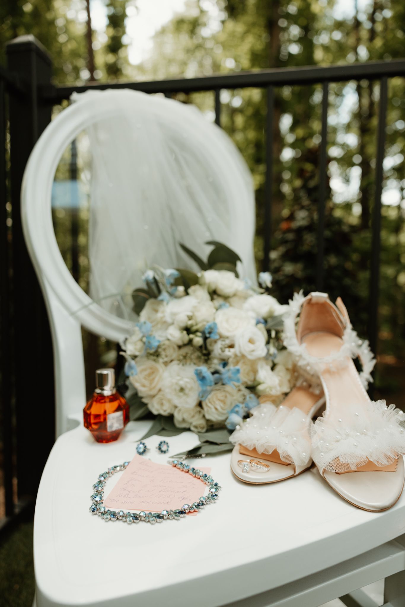 Wedding styling details with bridal shoes, perfume bottle, and blue and white floral bouquet on white vanity table.