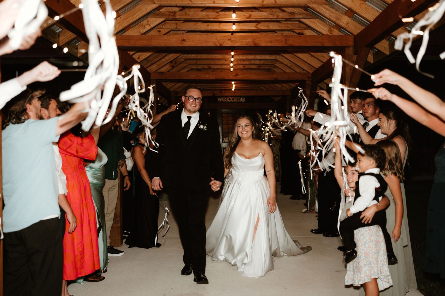 Wedding guests dance and celebrate on a rustic wooden dance floor while white streamers hang from the ceiling above.