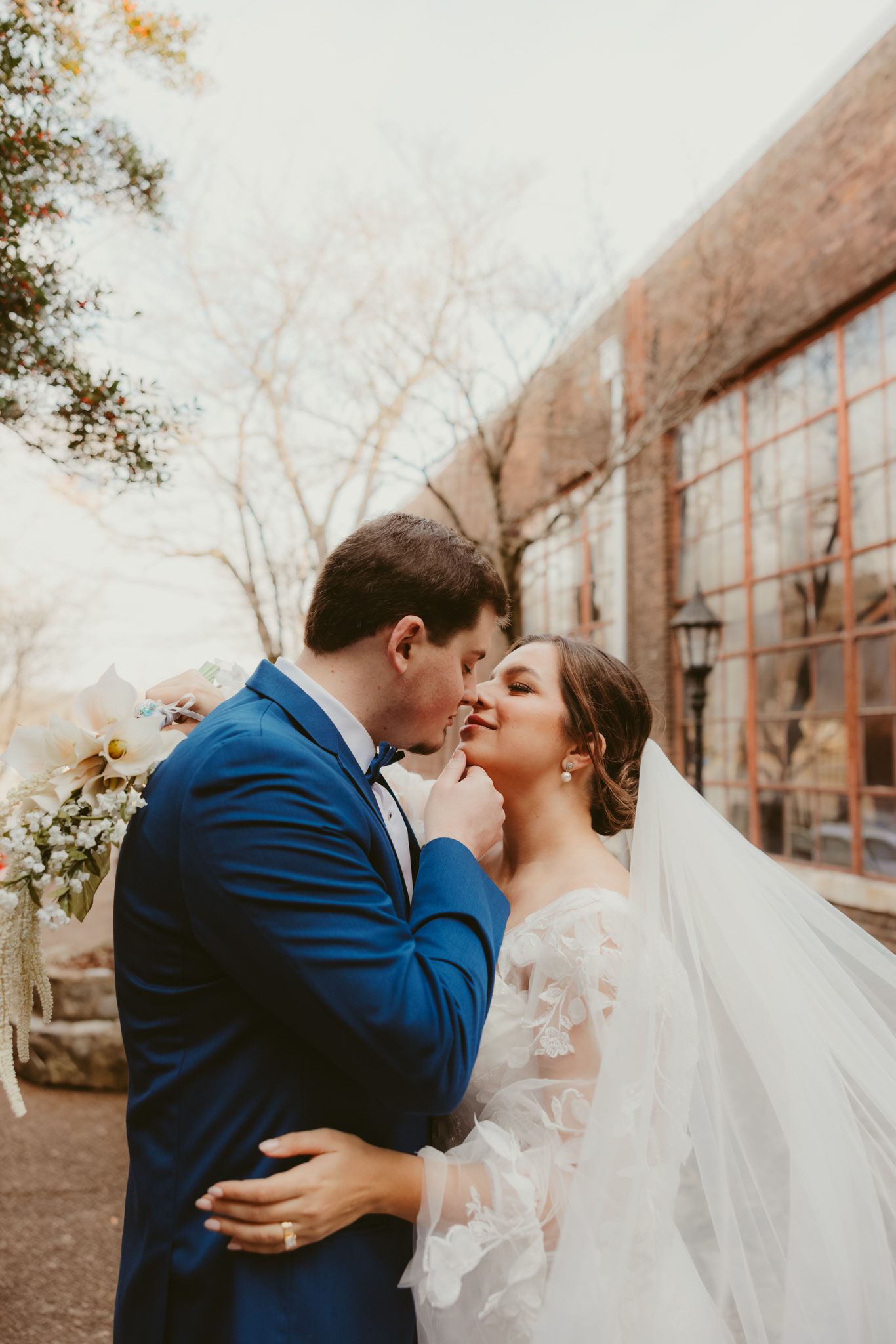 Romantic wedding portrait of couple embracing outdoors near brick building.