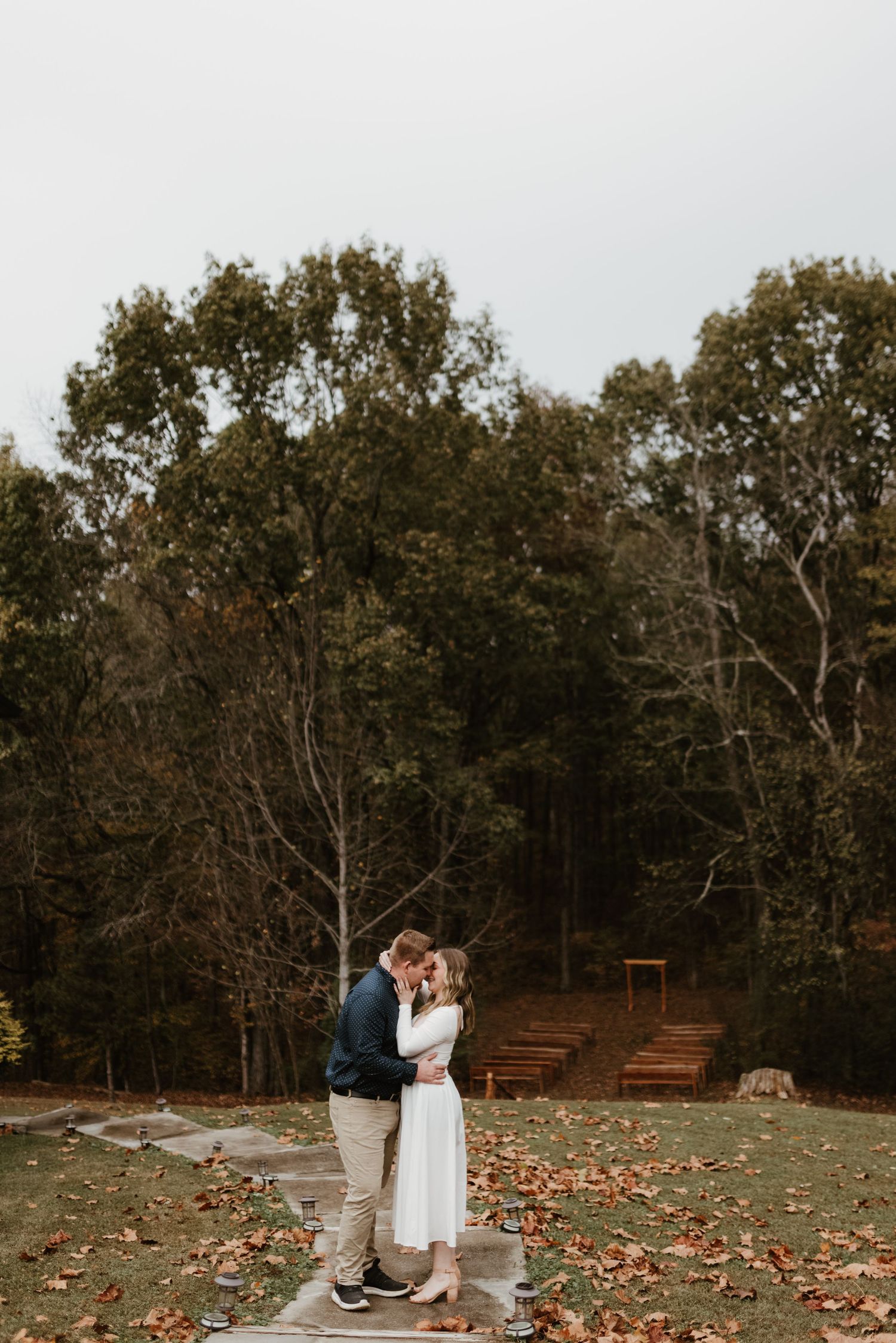 An intimate moment captured on a stone pathway with fall foliage and trees in the background.