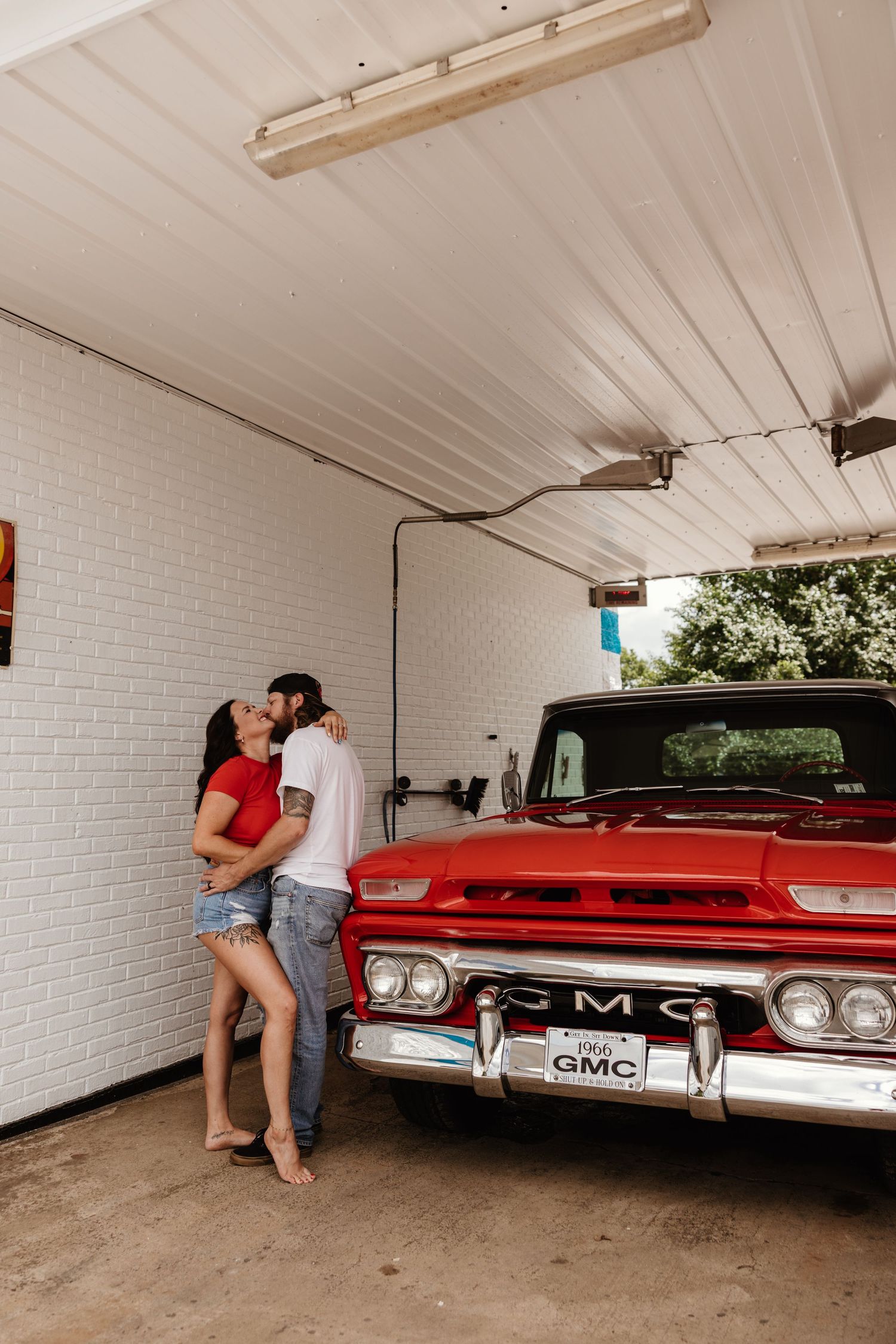 Couple sharing a romantic moment against a vintage red GMC truck in a garage.