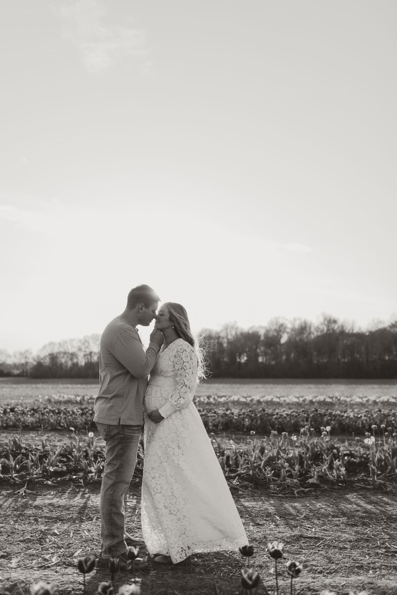 Romantic couple poses together in a winter field at sunset creating silhouettes against the sky.