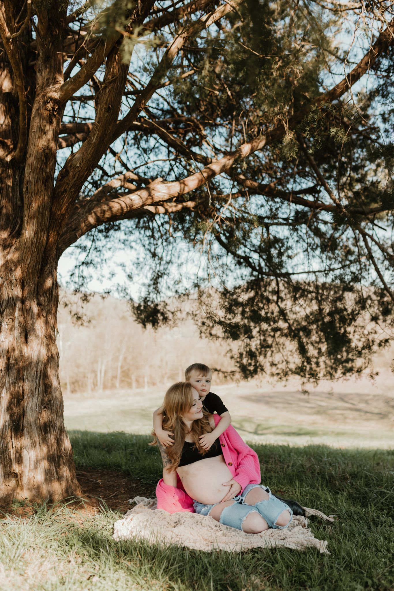 Couple relaxes together under large trees in a peaceful meadow setting.
