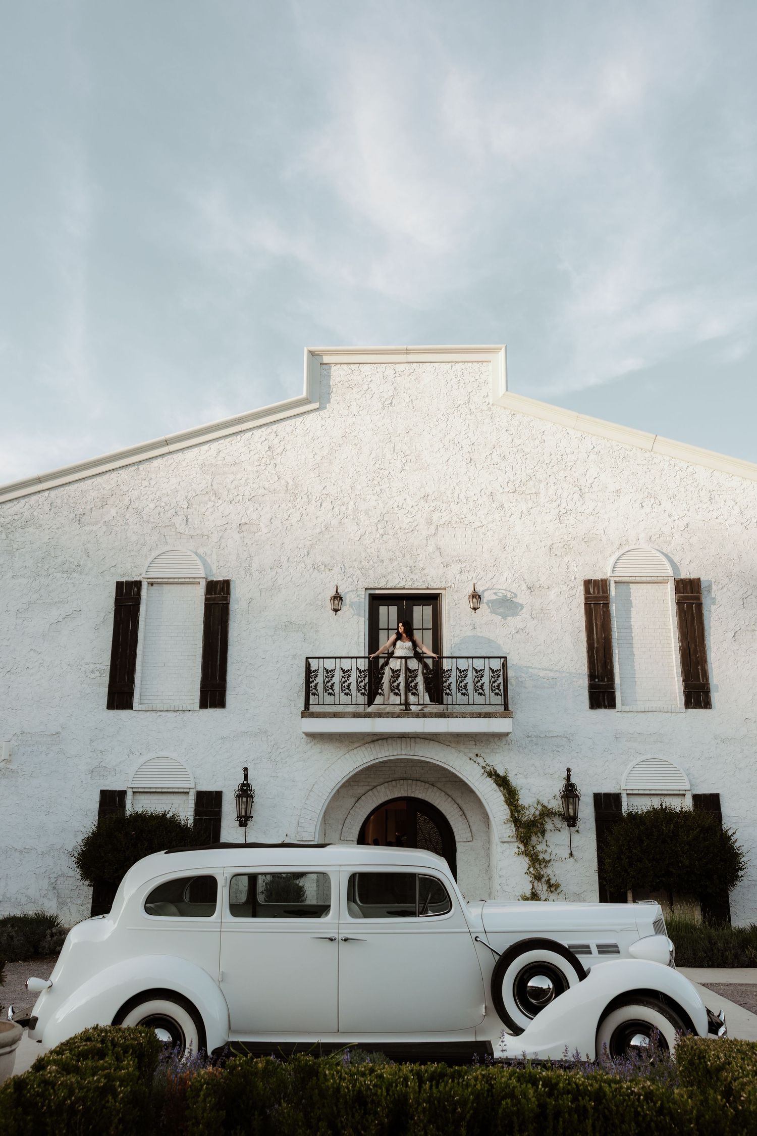 Classic white vintage car parked in front of an elegant white stucco wedding venue building.