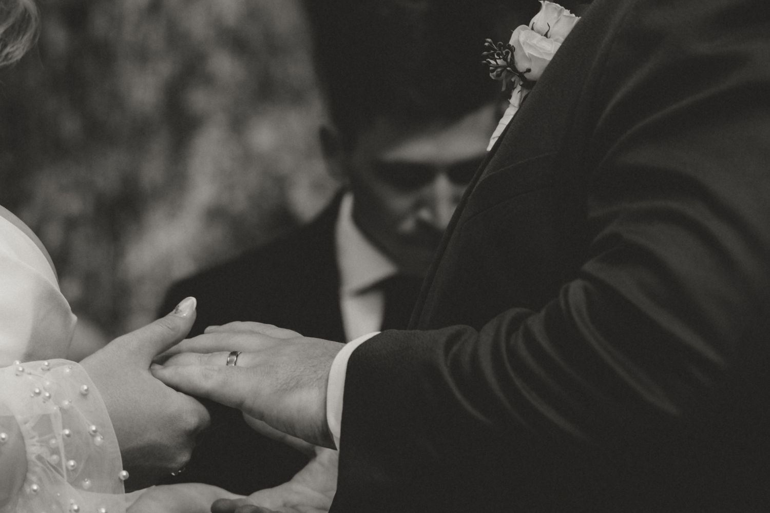 Black and white closeup of hands during an emotional wedding ceremony moment.