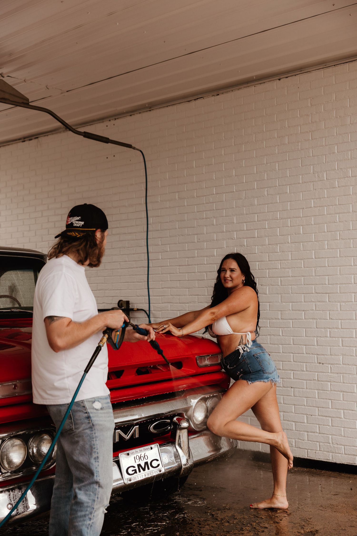 A playful car wash photoshoot featuring a vintage red GMC truck and white brick walls.