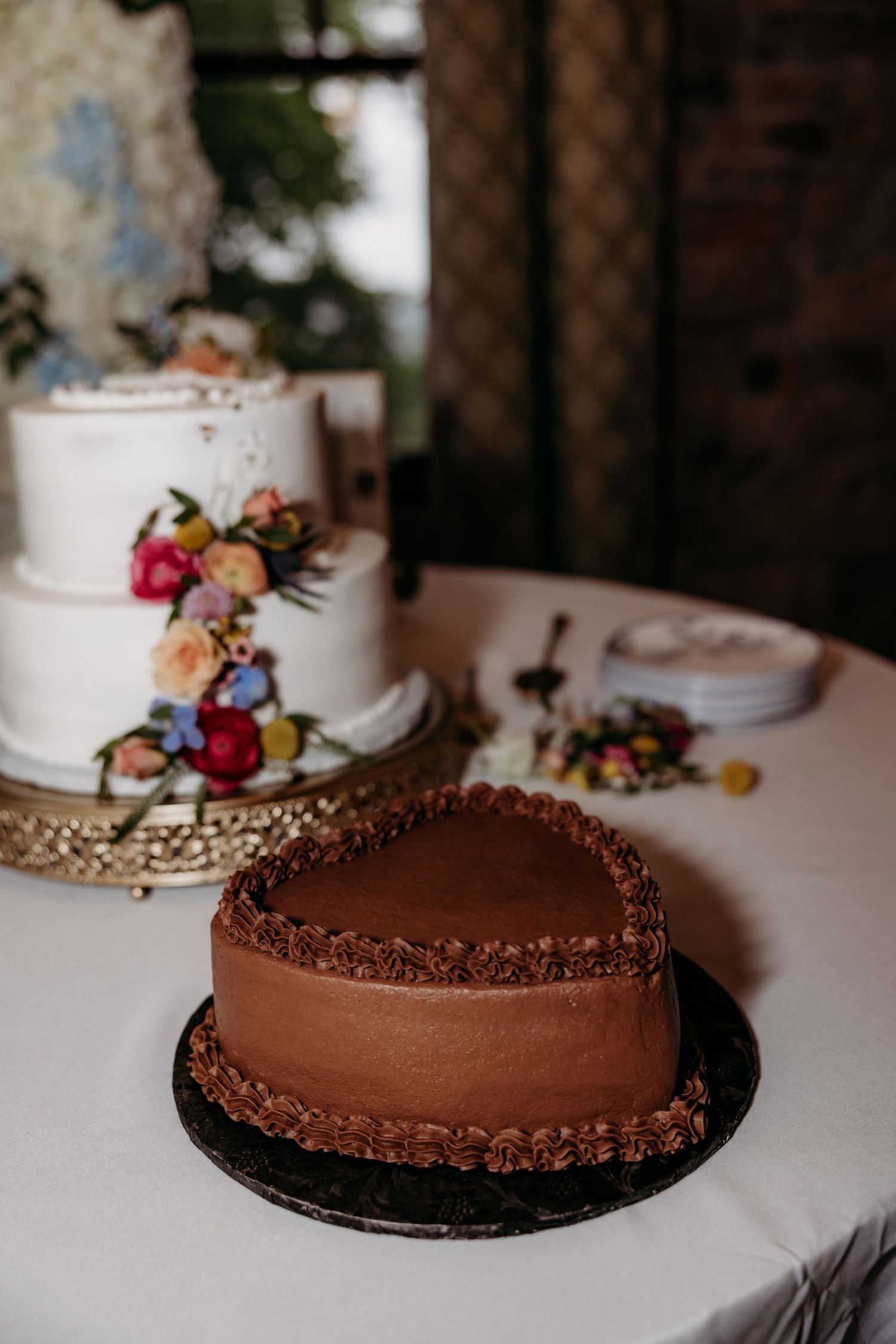 Wedding dessert table with chocolate cake and white tiered cakes decorated with colorful flowers.