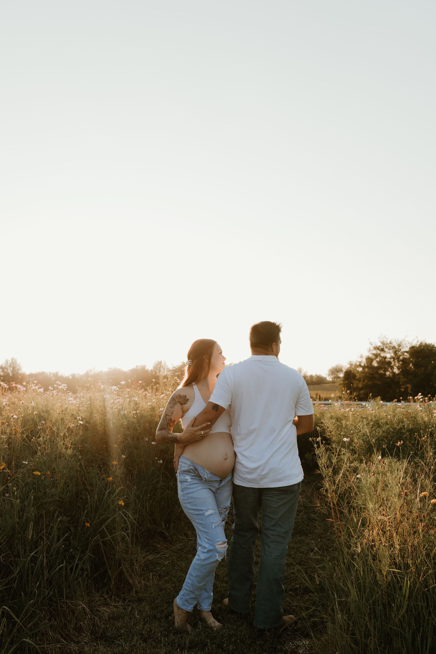 A couple walks together through a golden field at sunset creating a romantic silhouette against the glowing sky.