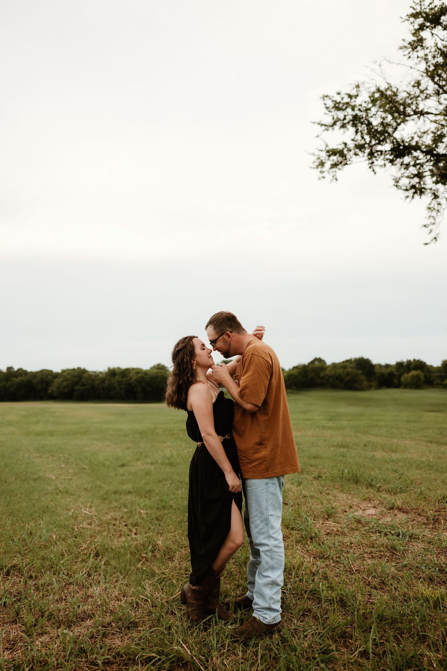 Romantic couple shares tender moments in a serene meadow at sunset with trees in the background.