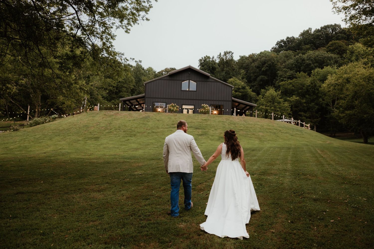 Romantic outdoor wedding photography session captures couple walking hand in hand across a lush green field.