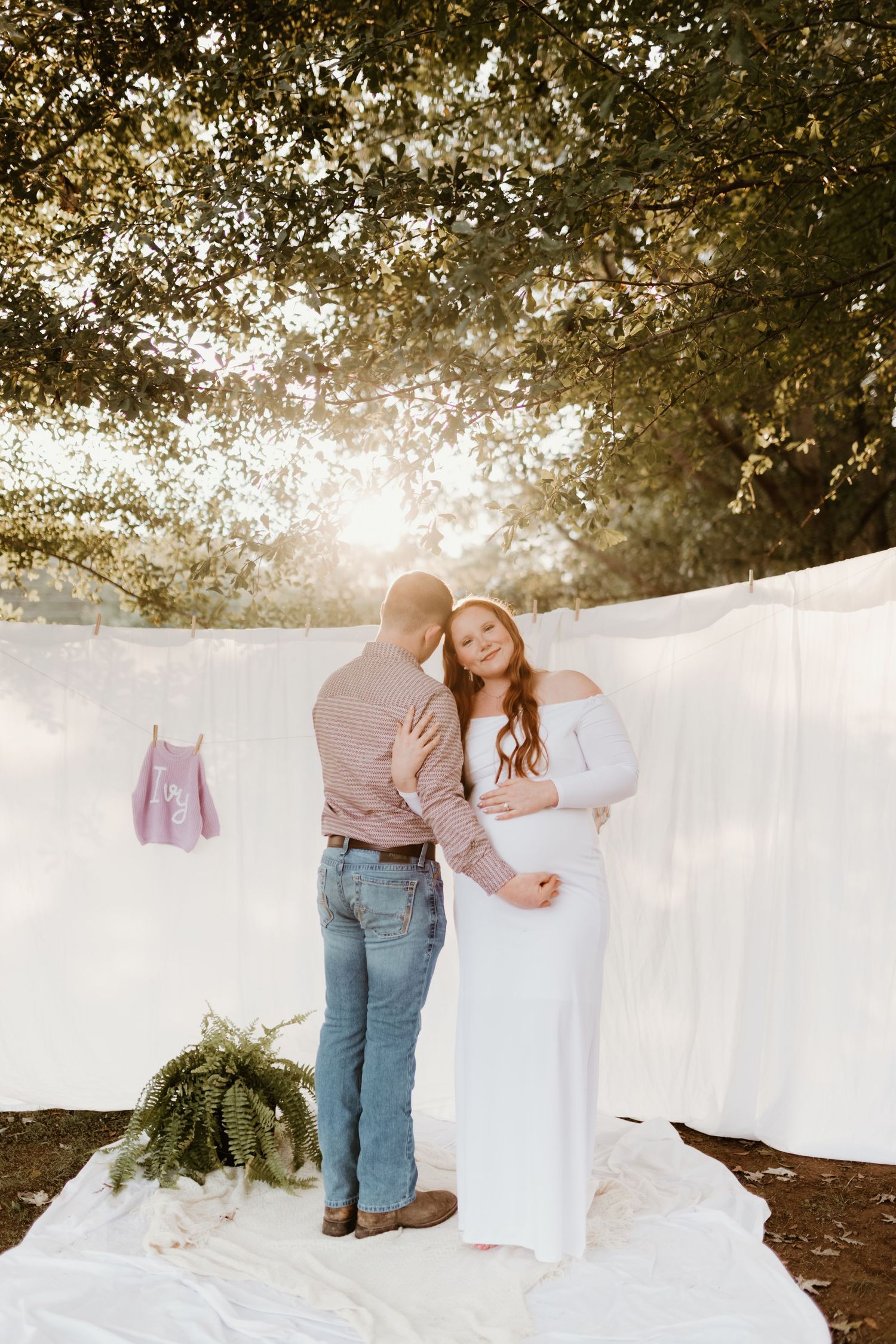 A romantic outdoor photo shoot with white fabric backdrop and greenery captured during golden hour sunset.