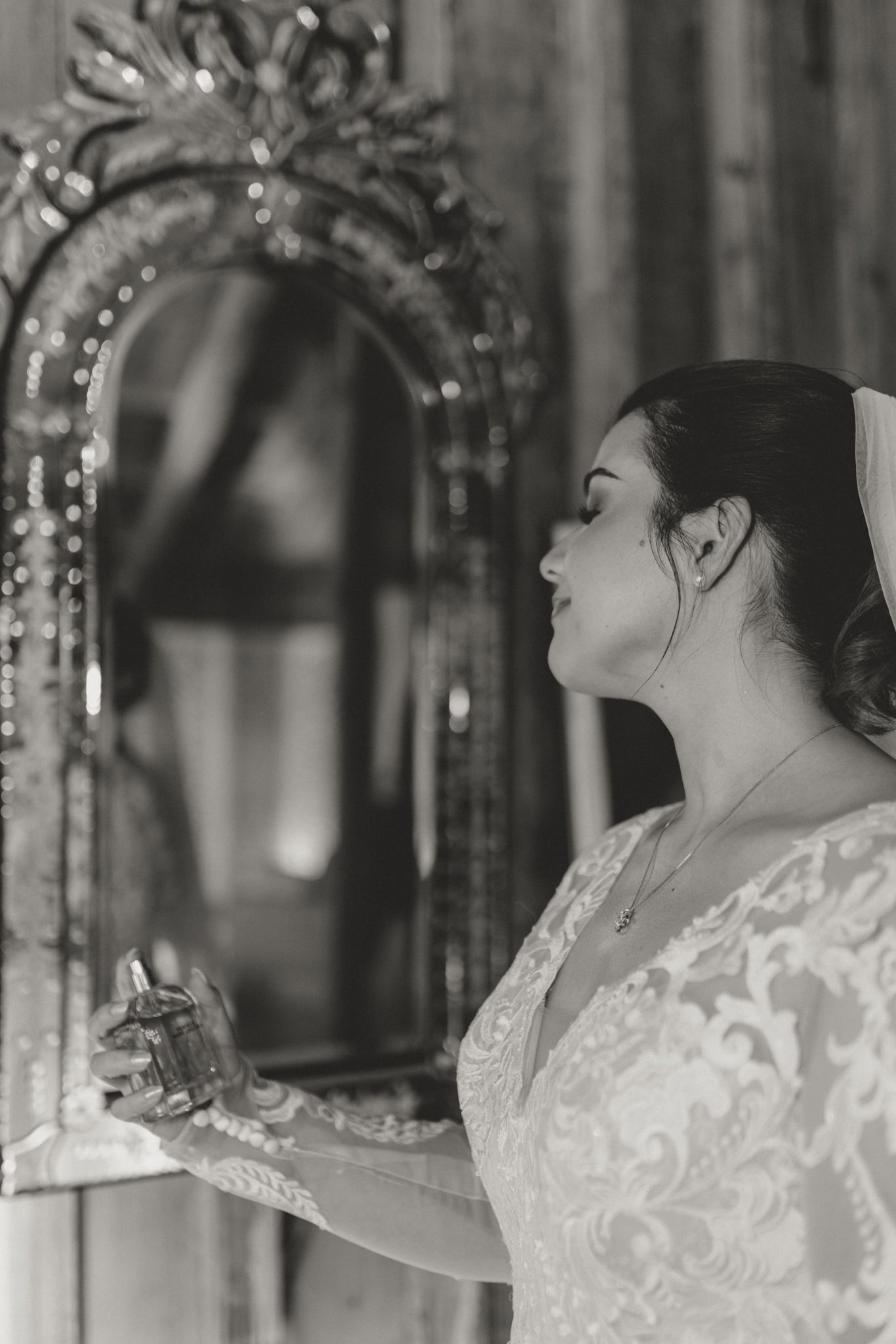 A bride wearing lace gazes at her reflection in an elegant ornamental mirror.