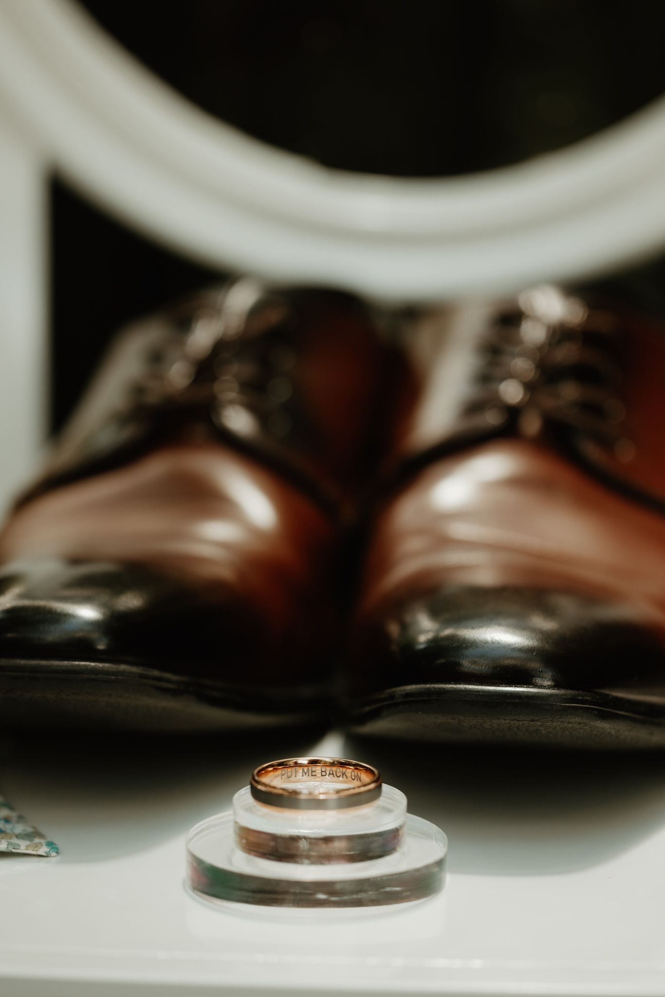 Wedding rings elegantly stacked in front of polished brown leather dress shoes in a stylish wedding detail photo.