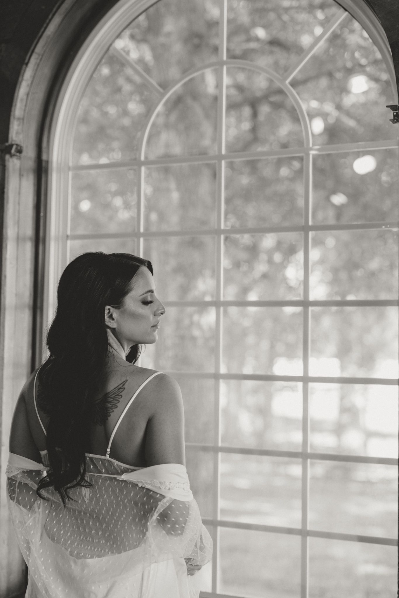 A wedding day portrait series of a bride looking contemplatively out a sunlit window in a lace gown.