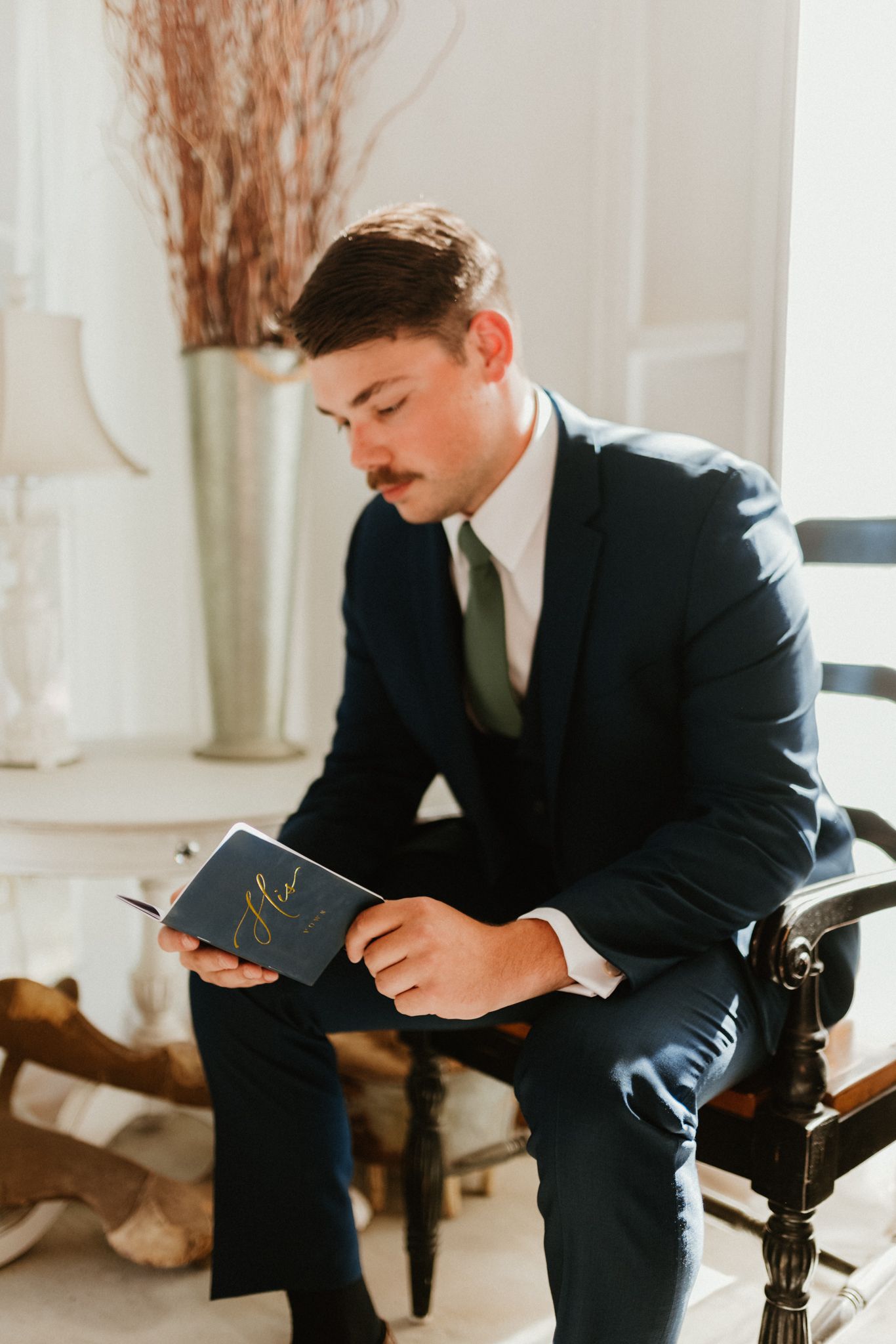 A groom in formal attire reading a letter while seated in an elegant room.