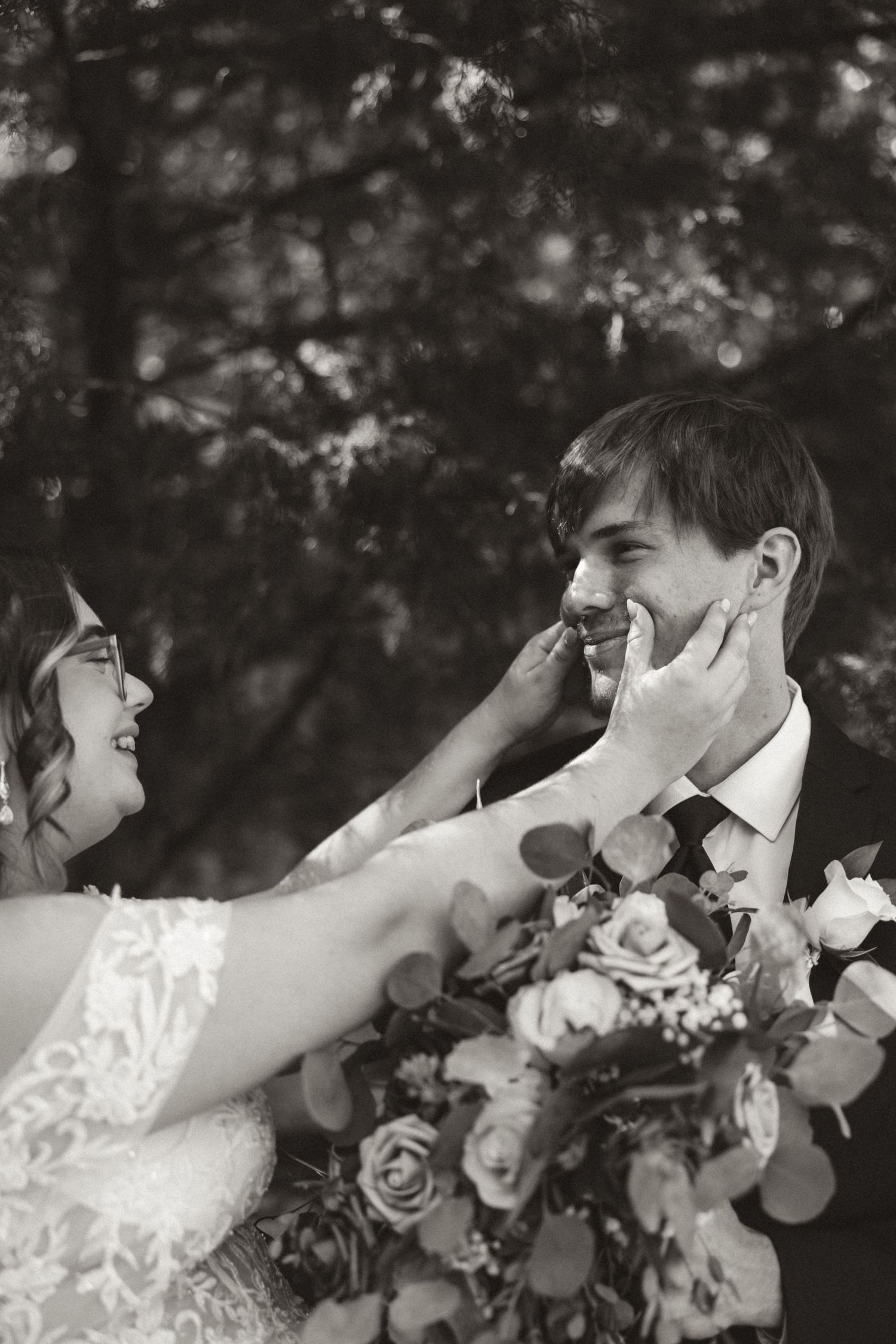 Black and white wedding photo showing a joyful candid moment between newlyweds holding a floral bouquet with roses.