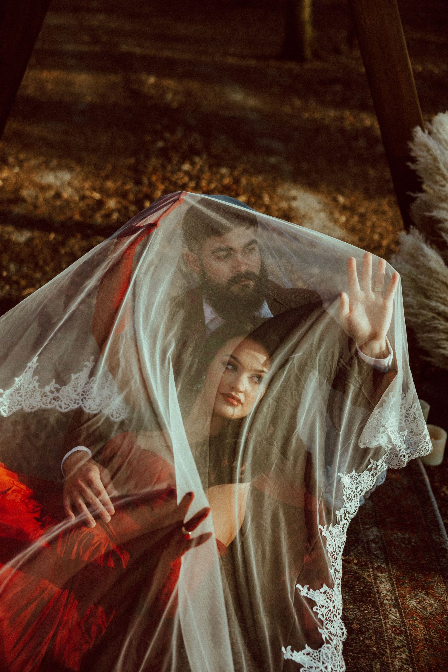 A couple shares a romantic moment under a lace veil during an outdoor wedding ceremony.