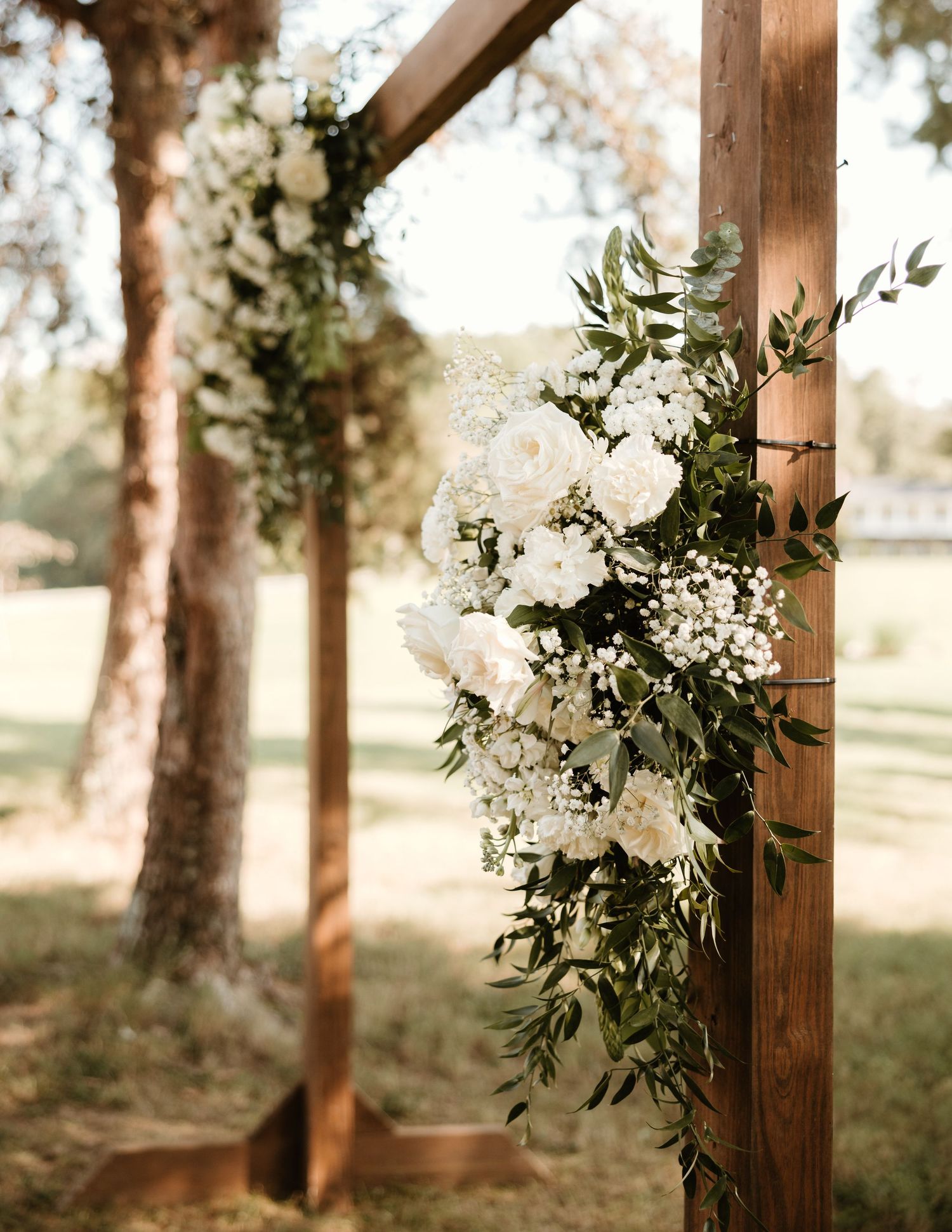 White floral wedding arch decoration with greenery and baby's breath on rustic wooden posts in an outdoor garden setting.