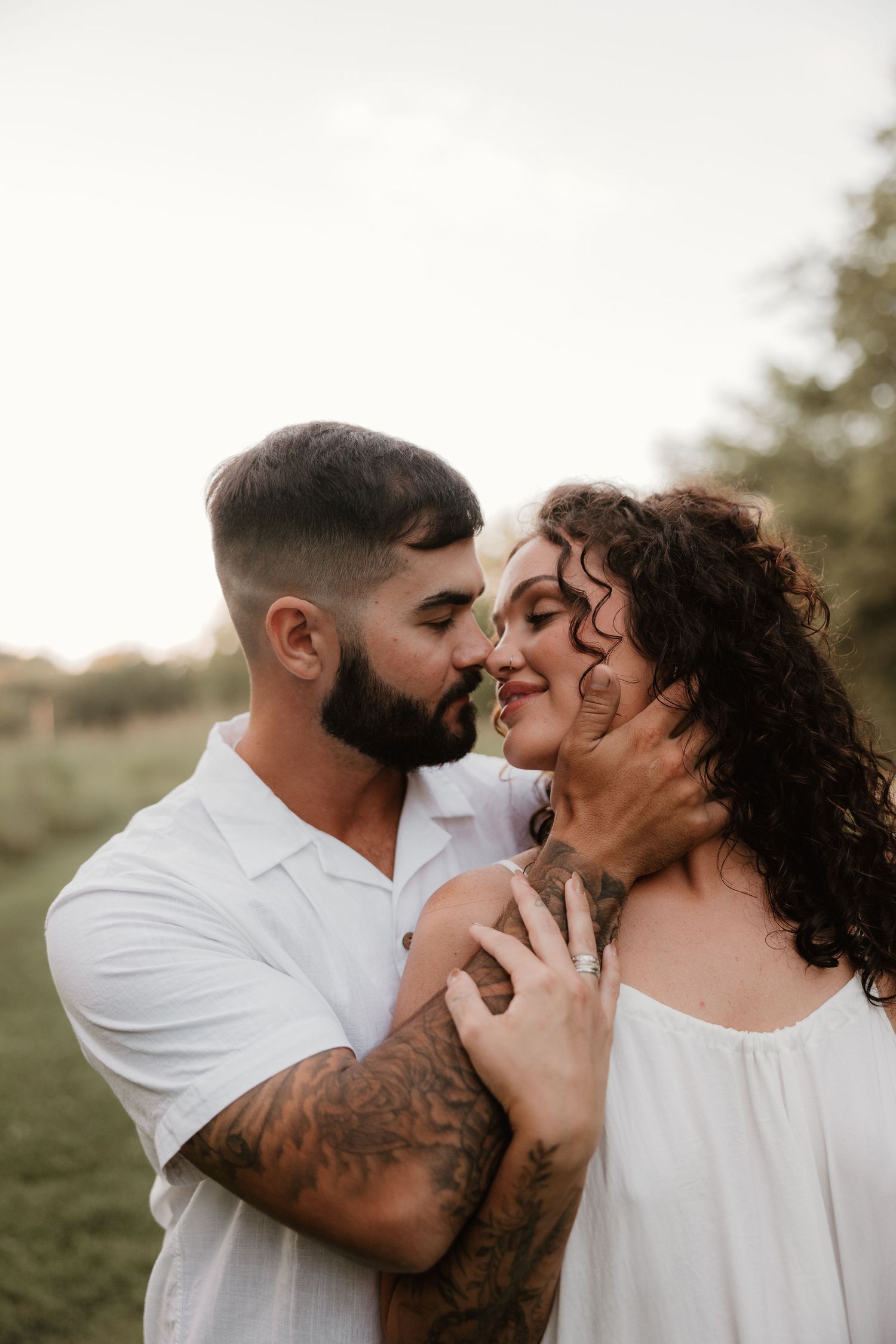 A romantic outdoor photo of a couple sharing an intimate moment in a natural setting at sunset.