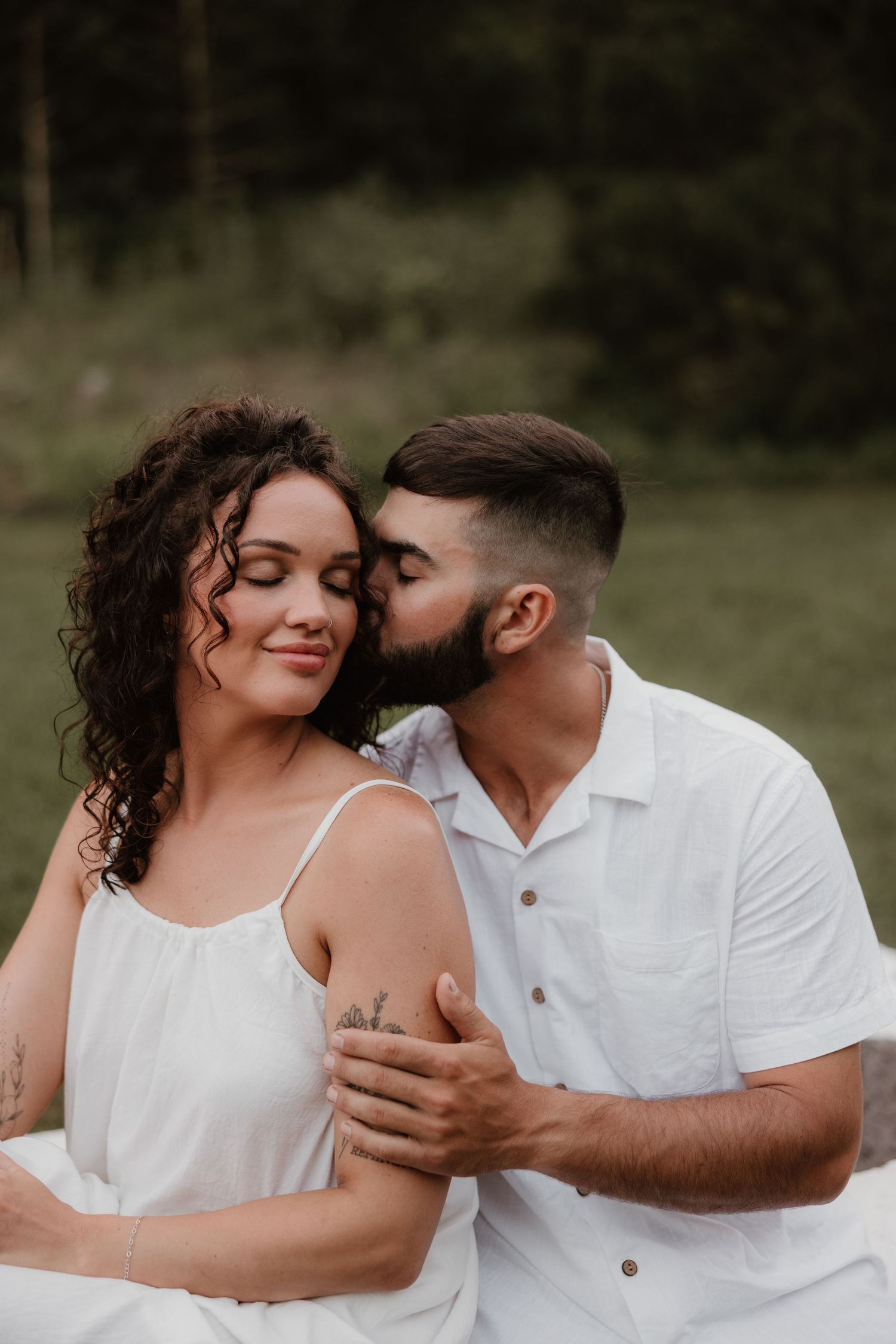 Intimate romantic moment between couple in white outfits against nature background.