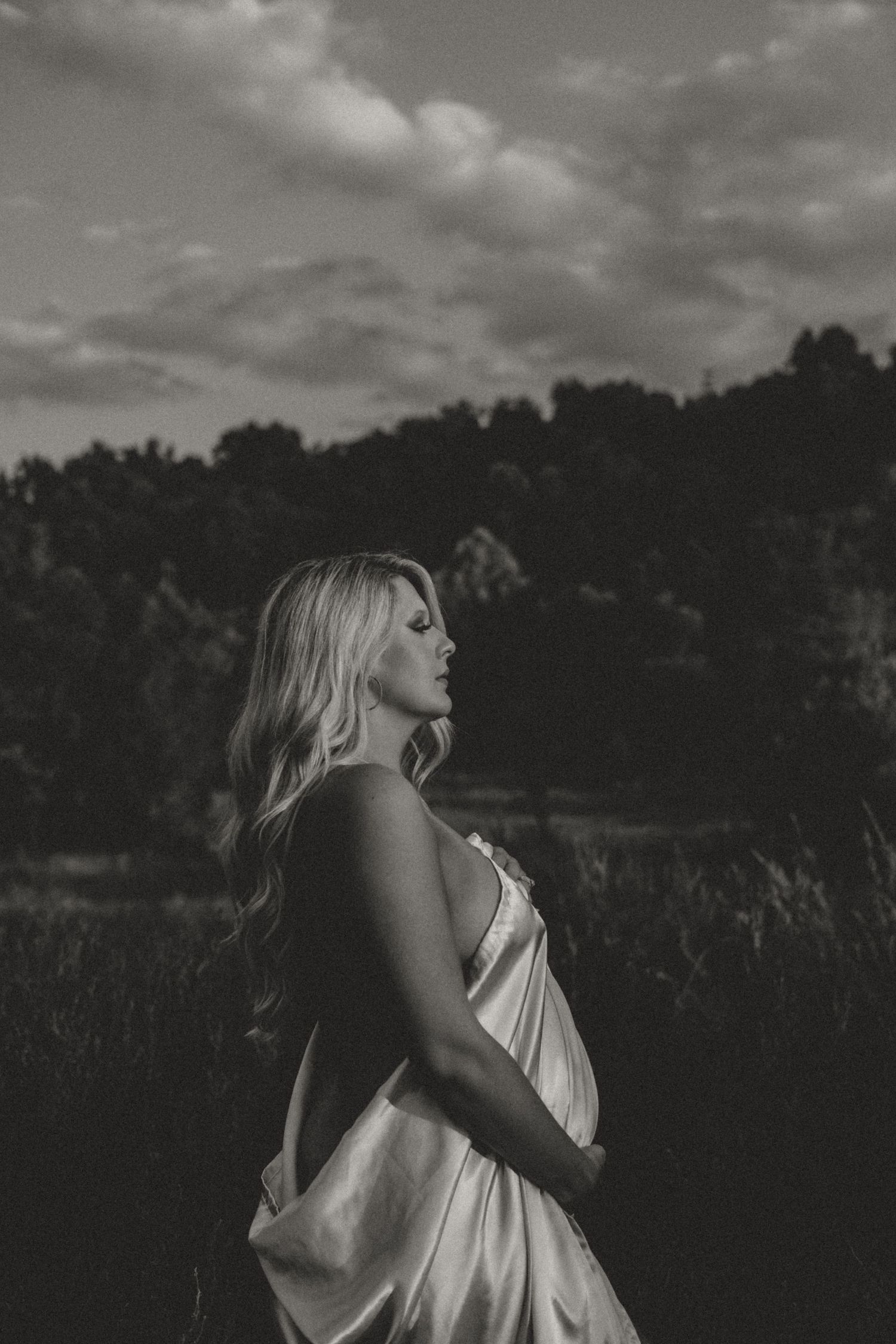 Black and white artistic portrait in a field with dramatic cloud backdrop.