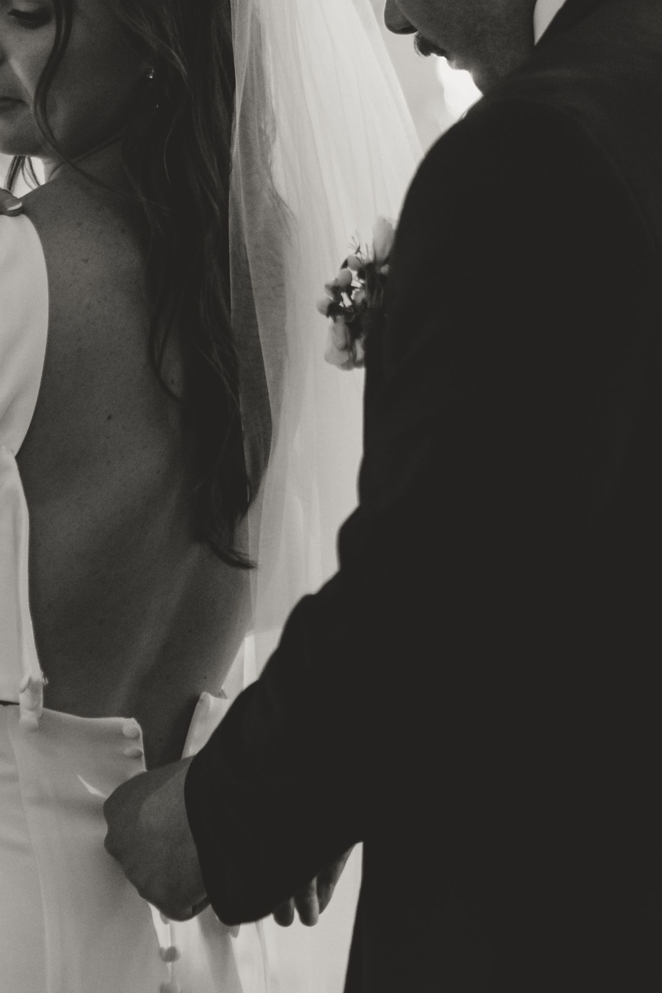 A black and white close-up shot of a couple holding hands during their wedding ceremony.