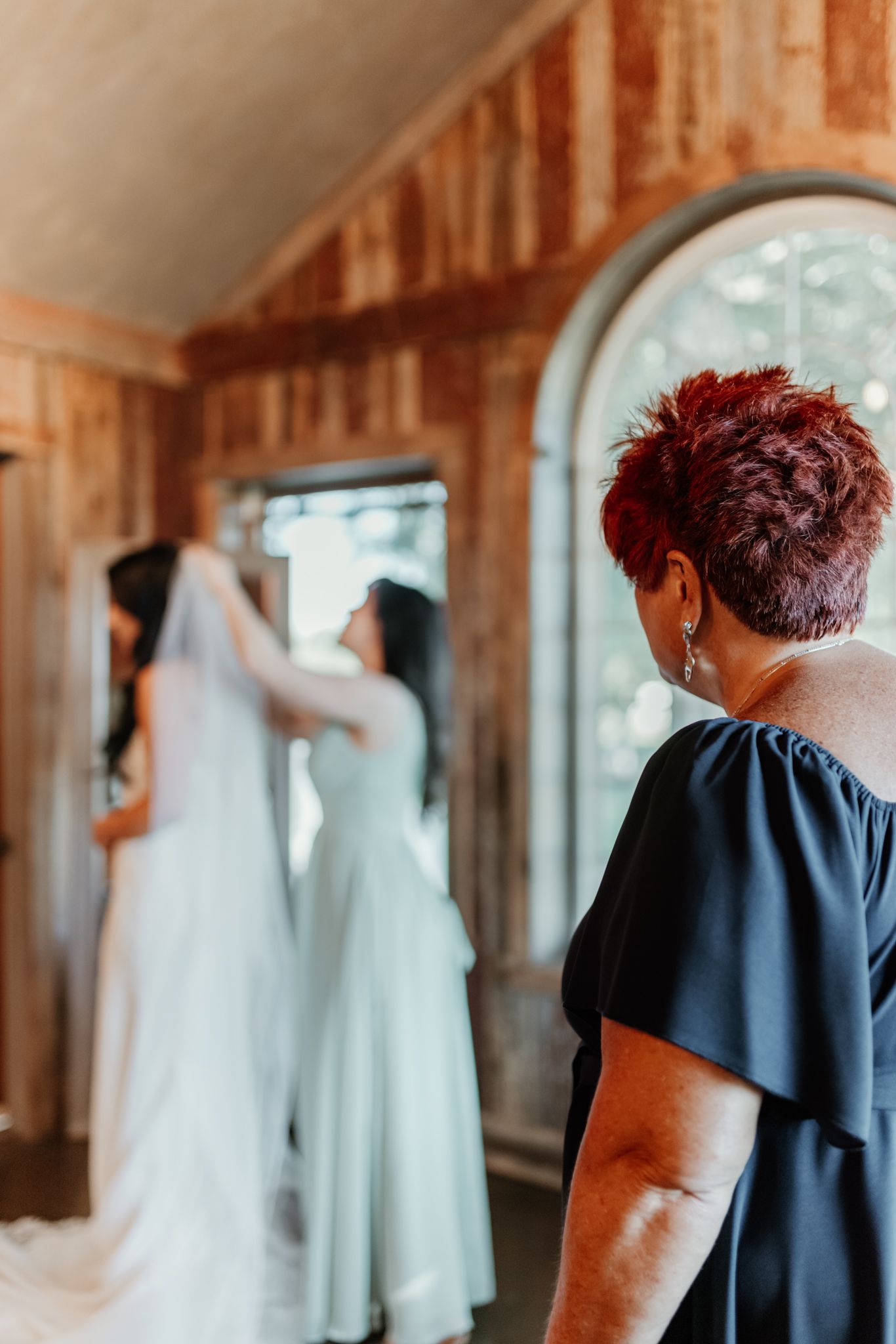 A series of wedding preparation photos showing someone admiring a white bridal gown hanging in a wooden room.
