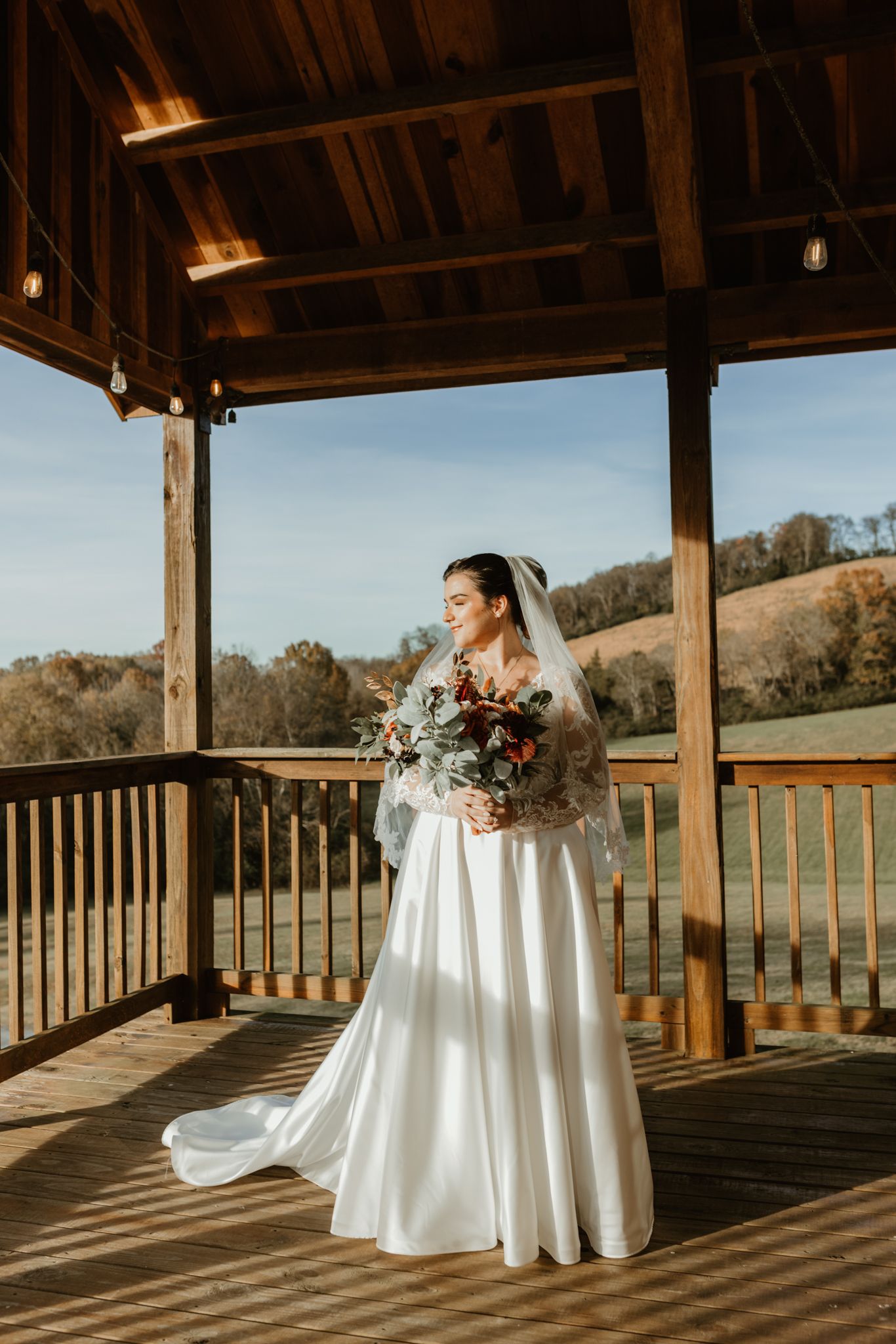 Sunlit wooden deck with a covered porch overlooking scenic rolling hills and countryside.