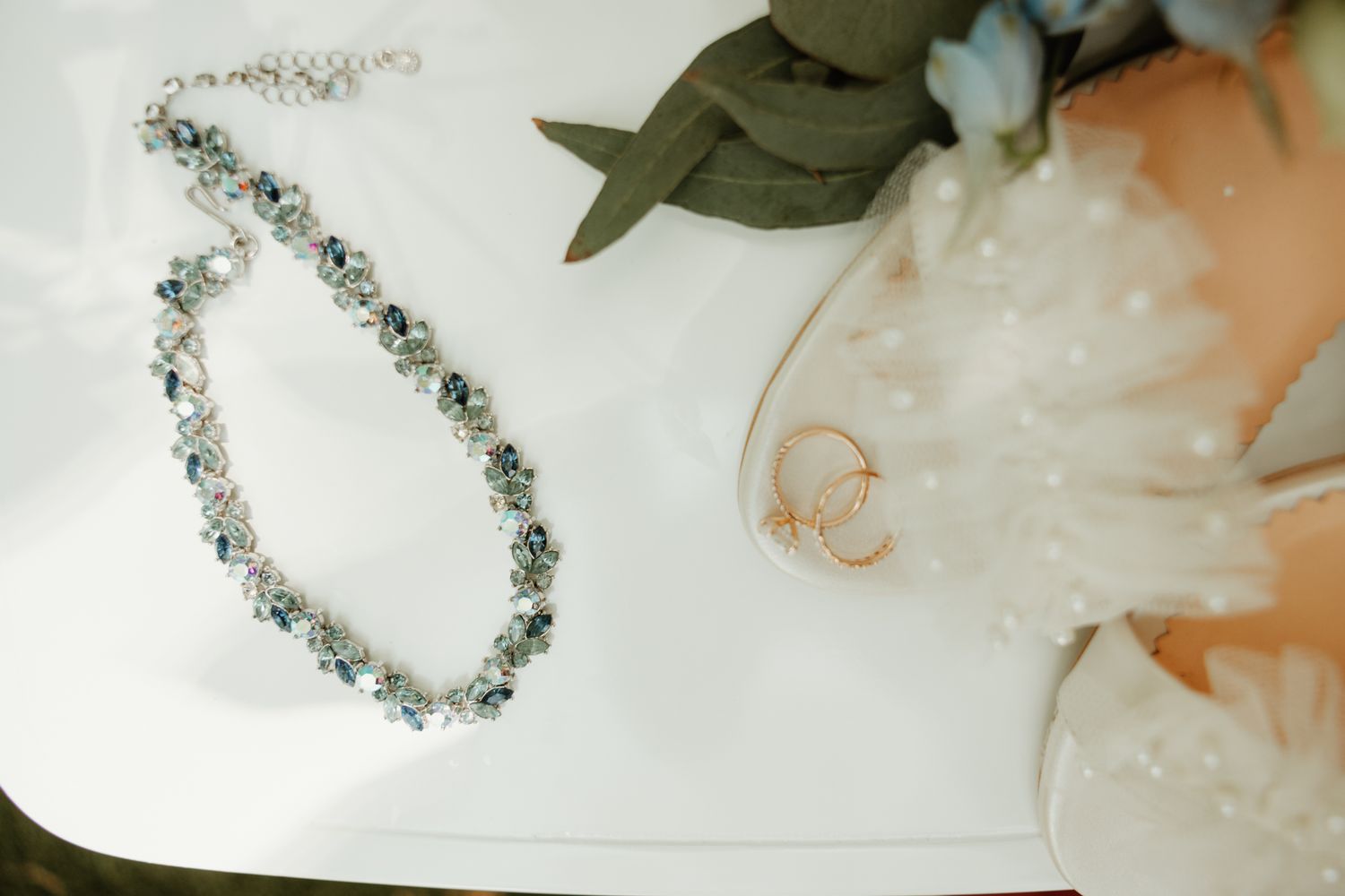 A delicate silver floral bracelet with crystal embellishments lies on a white surface next to soft peach-colored flowers.
