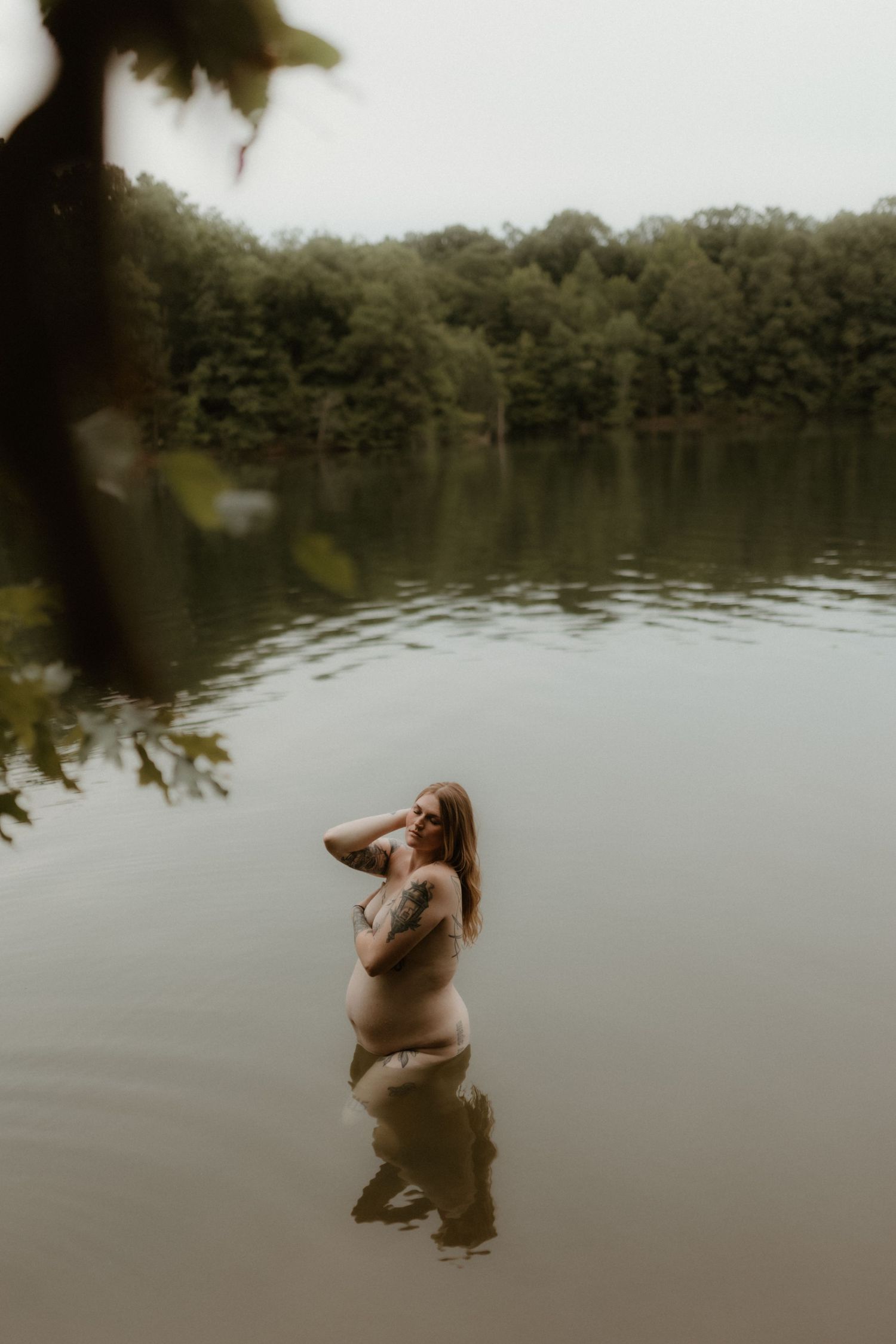 A sequence of photos showing a person wading deeper into a peaceful lake surrounded by trees on an overcast day.