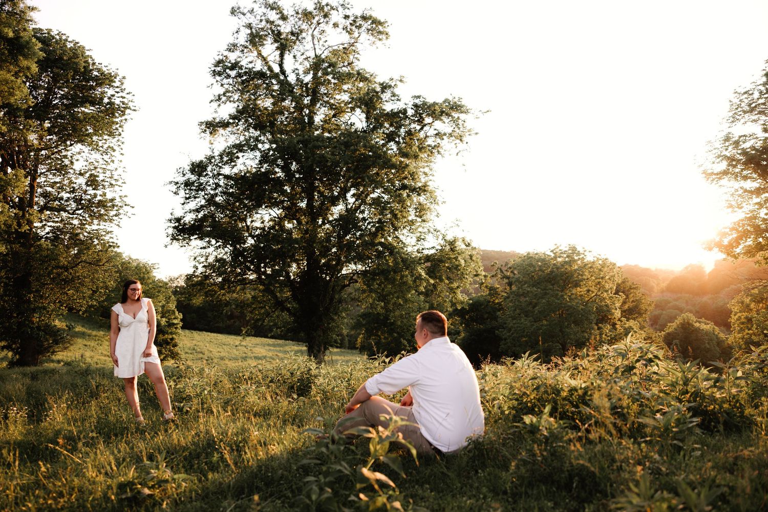 People enjoying a golden sunset in a grassy meadow with tall trees and wildflowers in the background.