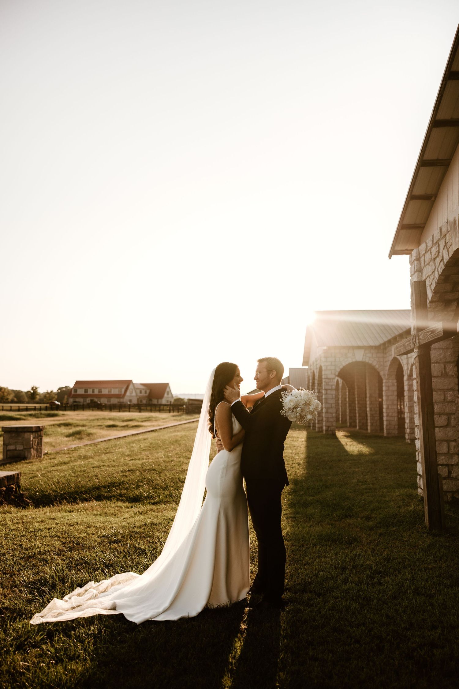 Silhouetted wedding couple poses in golden sunlight against a rustic architectural backdrop.