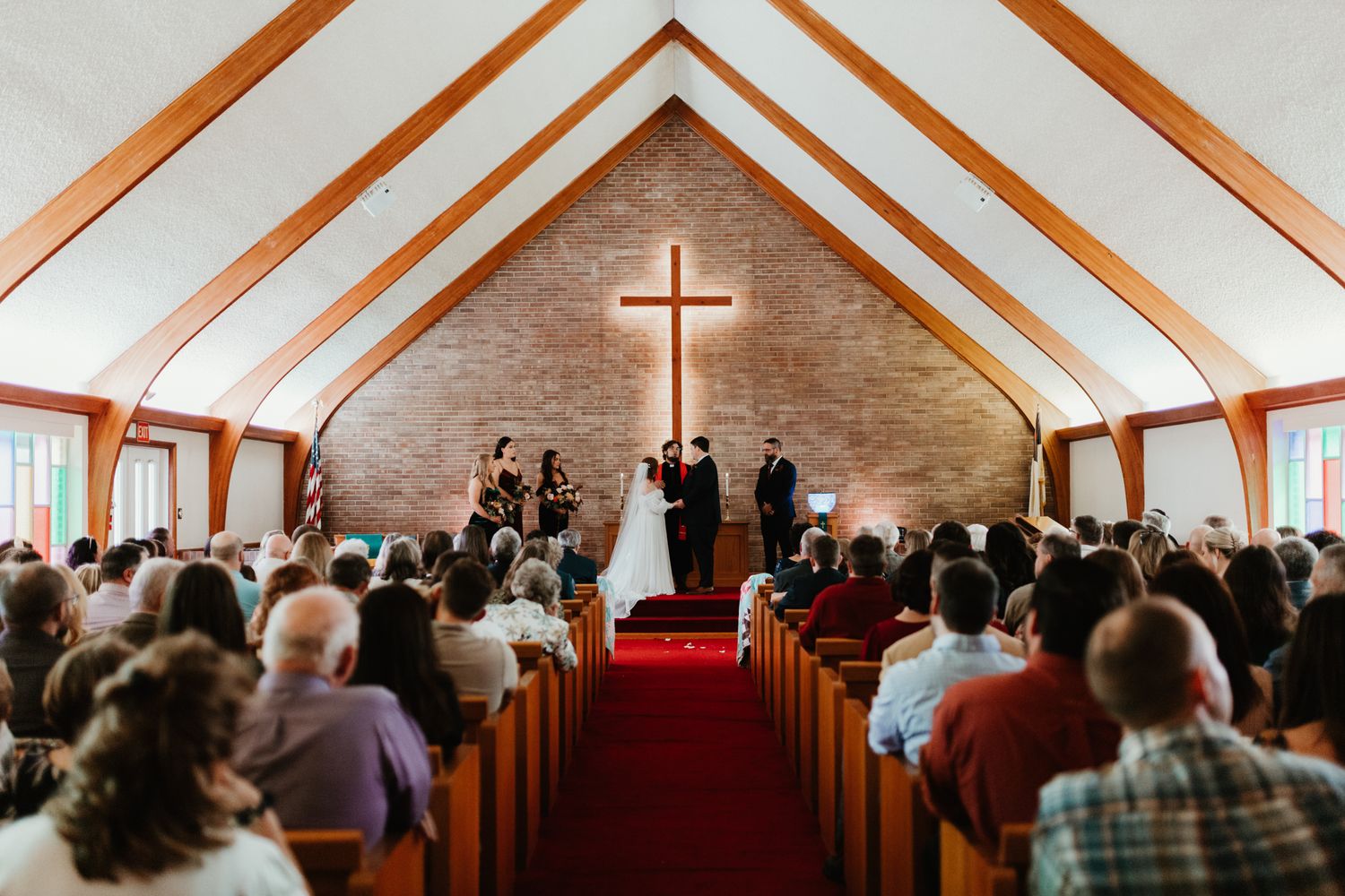 A traditional church wedding ceremony taking place in a chapel with wooden beams and a large cross at the altar.