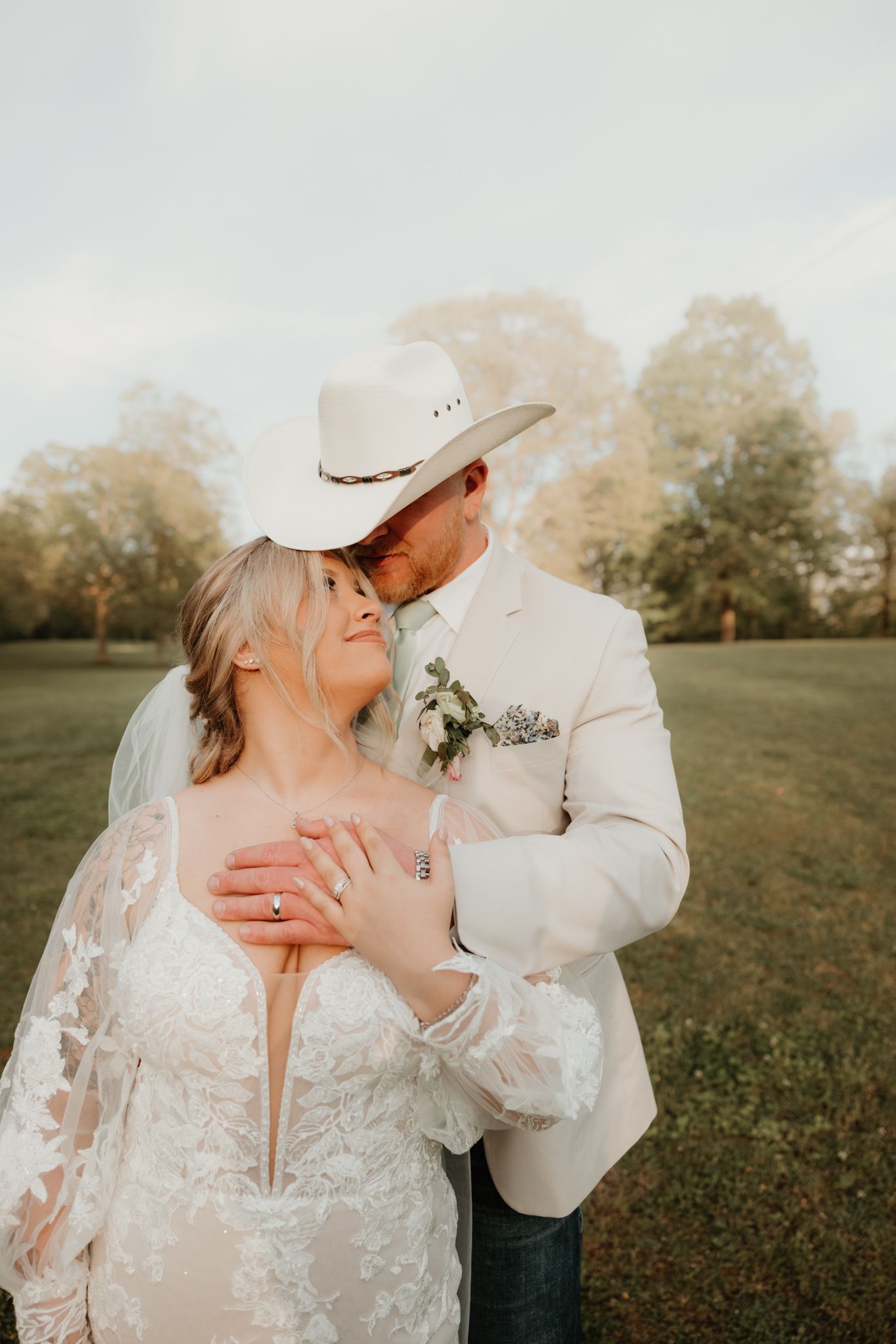Romantic outdoor portrait of couple in wedding attire with cowboy hat at sunset.
